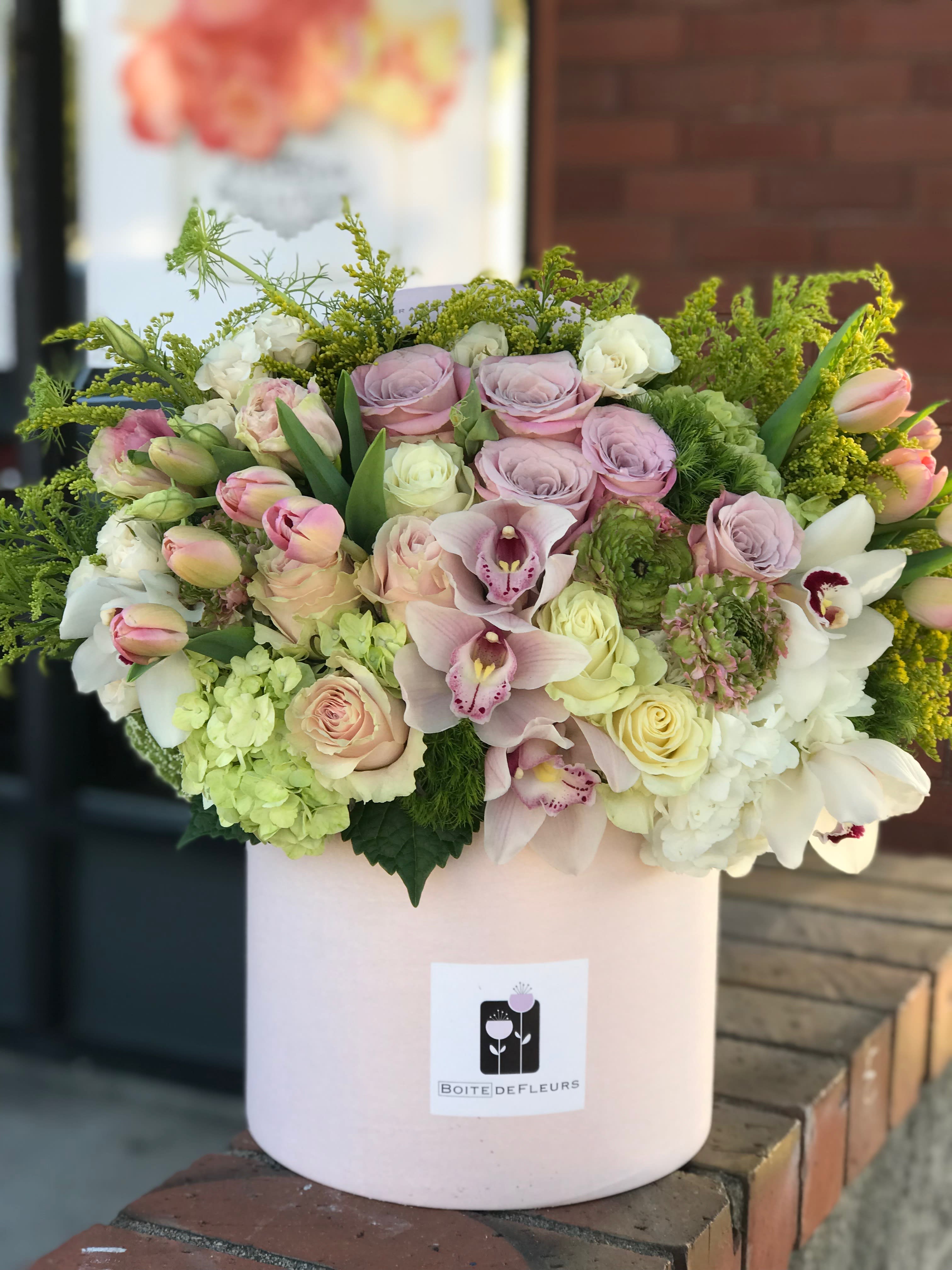 Pastel bouquet of roses, orchids, and hydrangeas in a pink hatbox