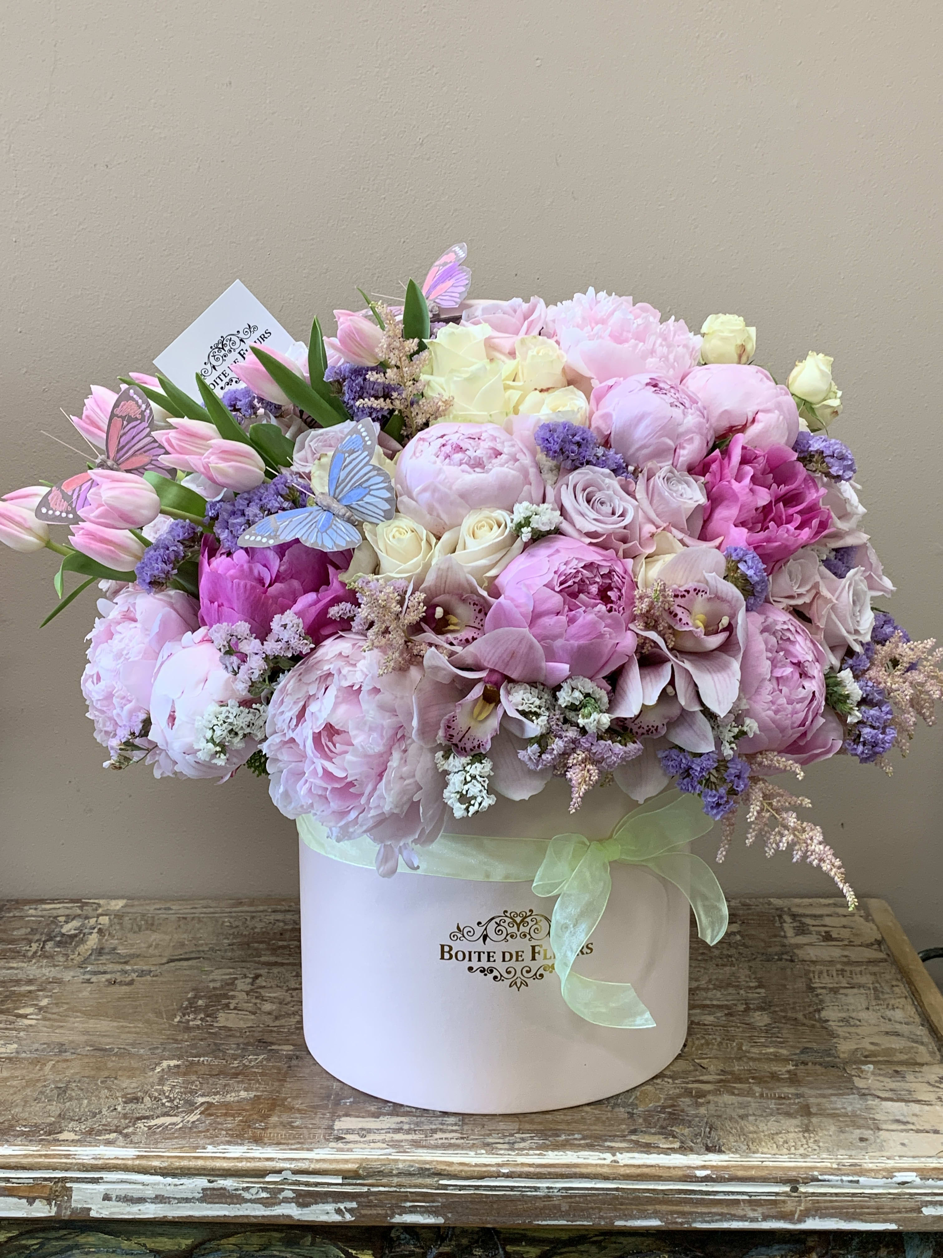 Pink and white floral arrangement in a round box with butterfly picks