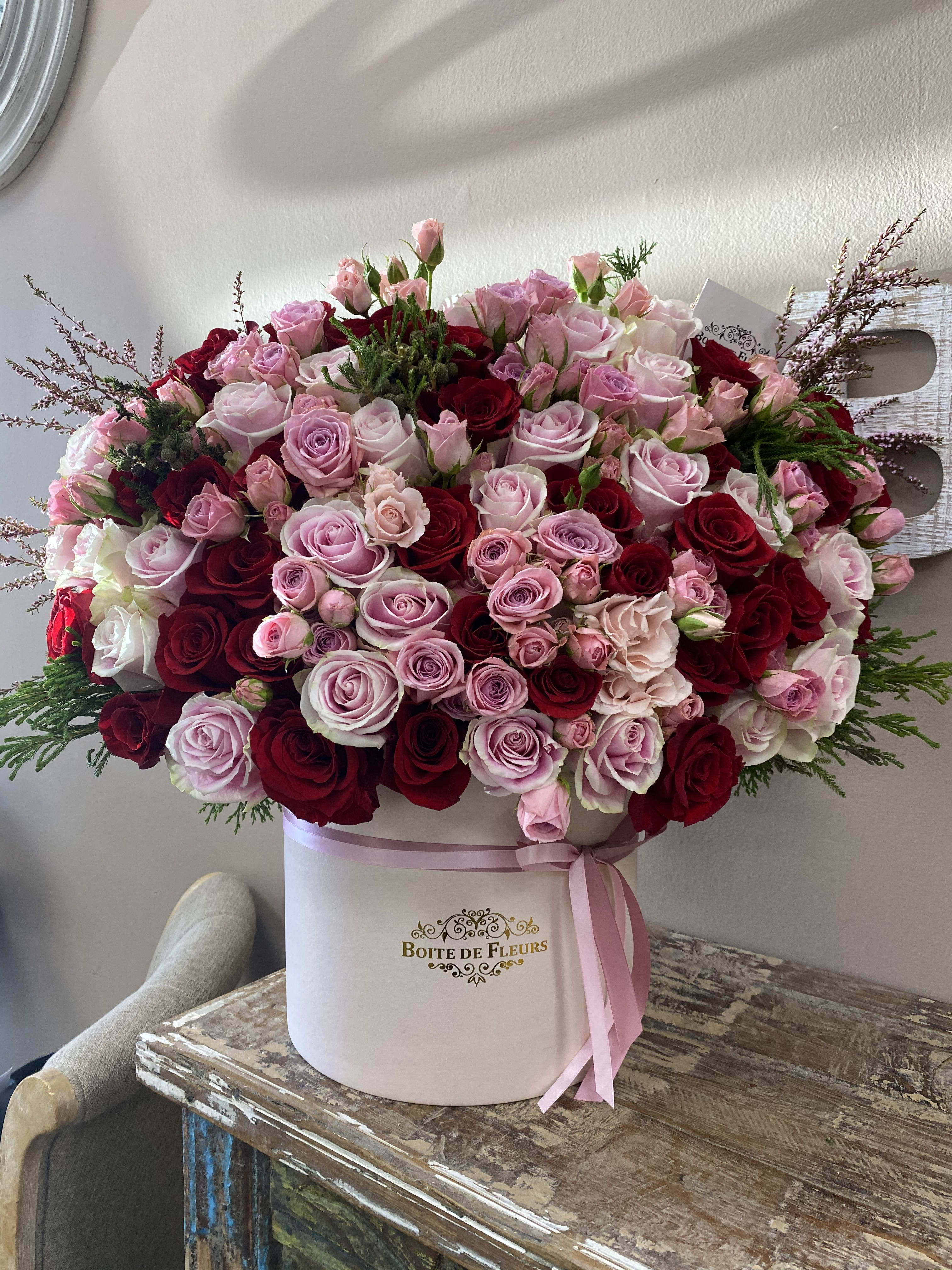 Large pink and red rose arrangement in a round hat box with ribbon