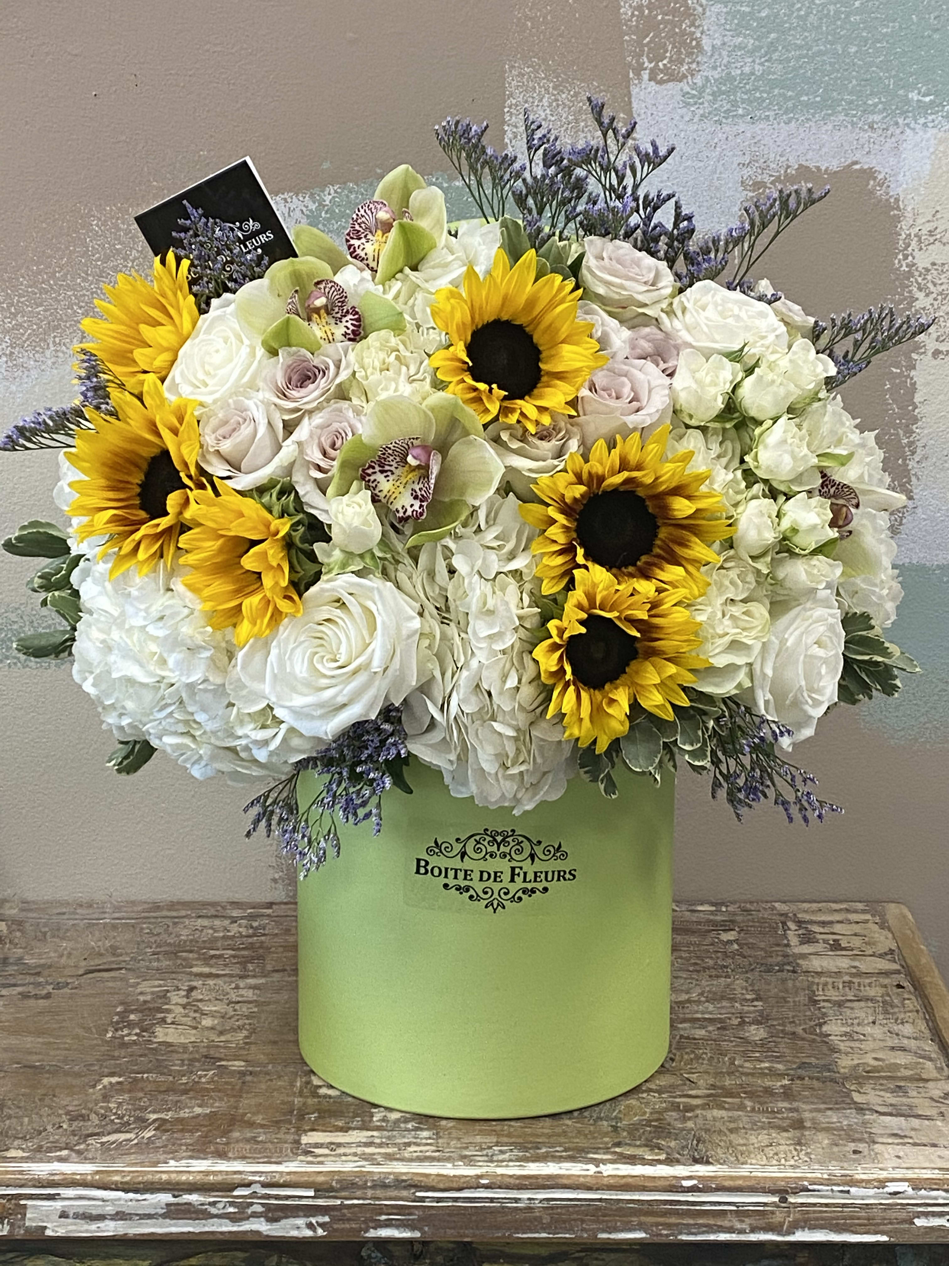 Mixed bouquet with sunflowers, white roses, and orchids in a green box