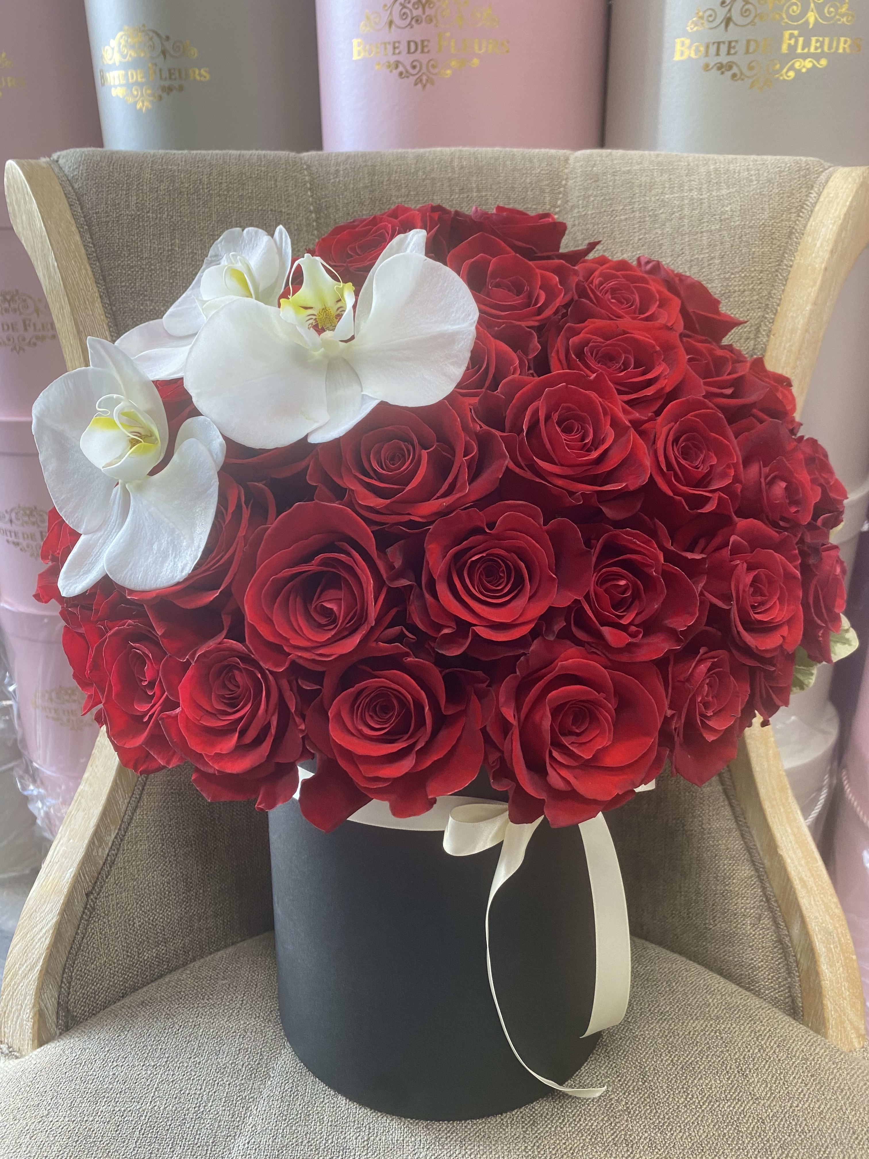 Red roses in a black hat box with white orchids and ribbon