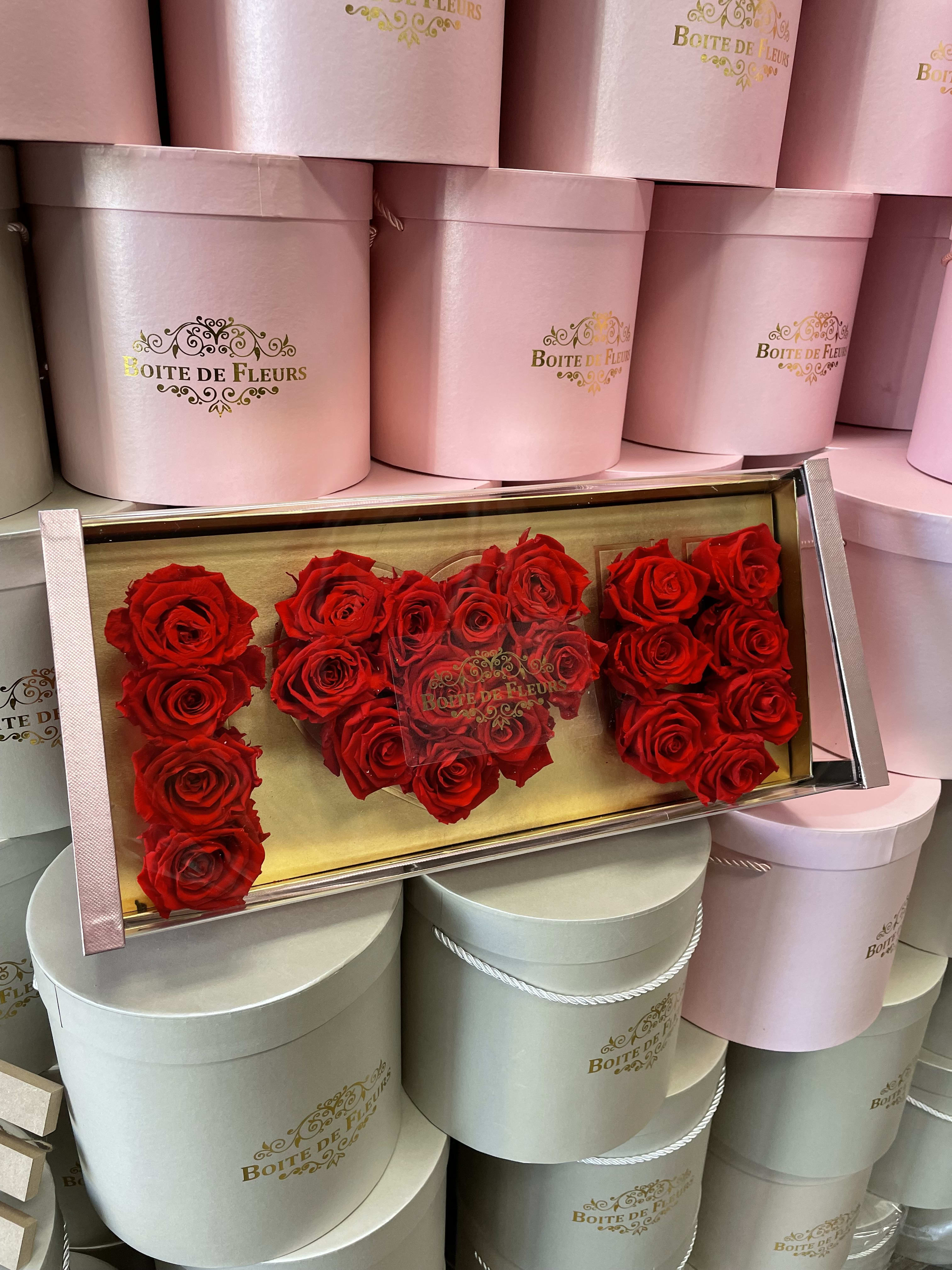 Red roses arranged in a clear rectangular box with pink round hat boxes behind
