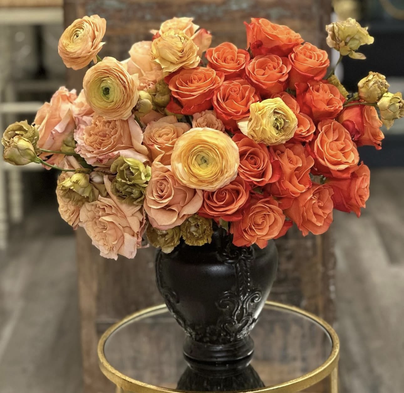 Bouquet of orange and peach roses with yellow ranunculus in a black vase