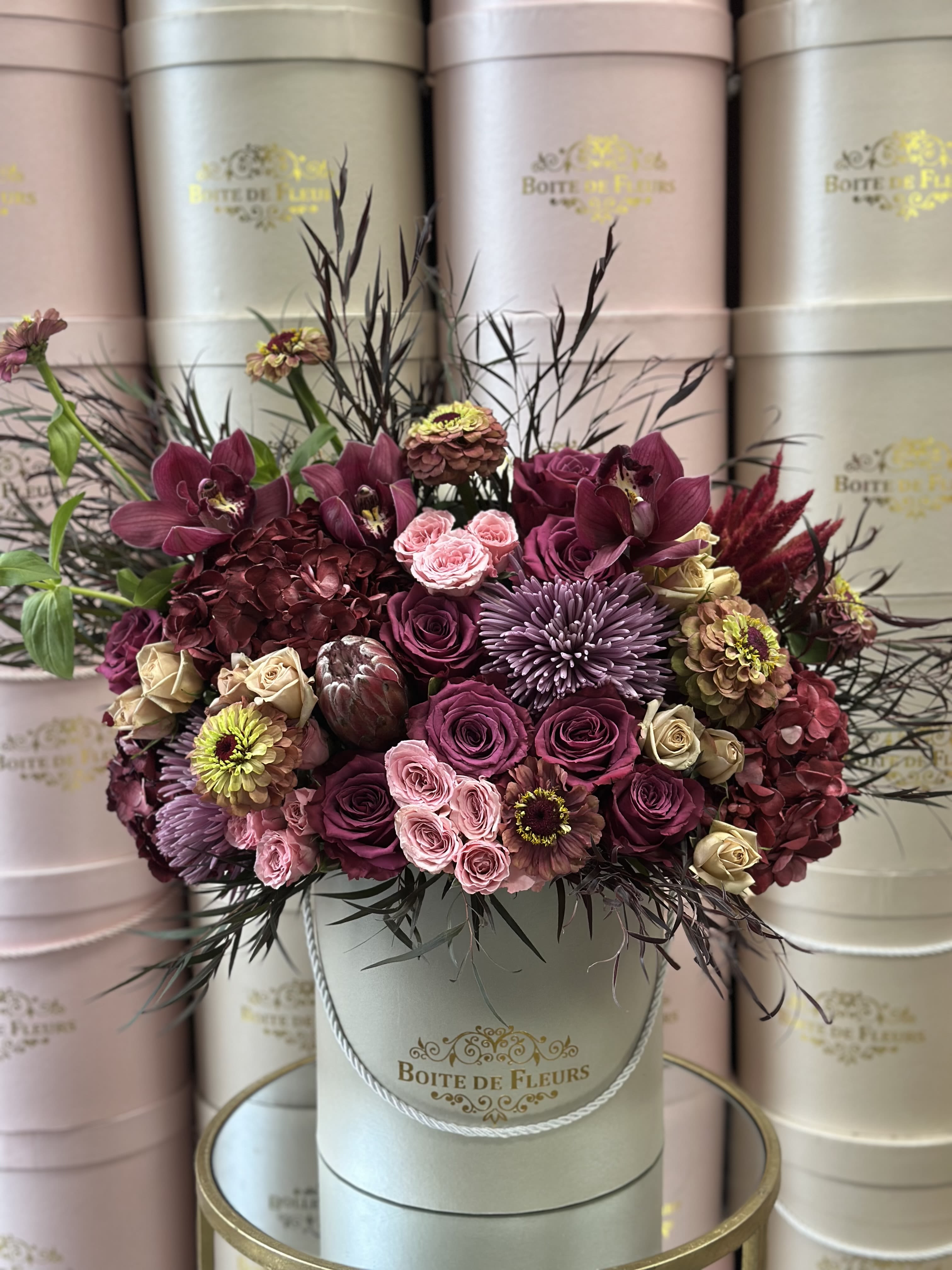 A burgundy and pink floral arrangement in a round hatbox.