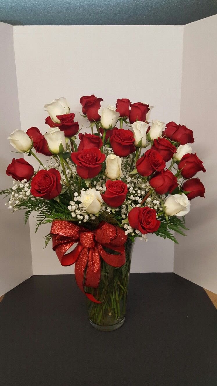Red and white roses arranged in a glass vase with a red ribbon