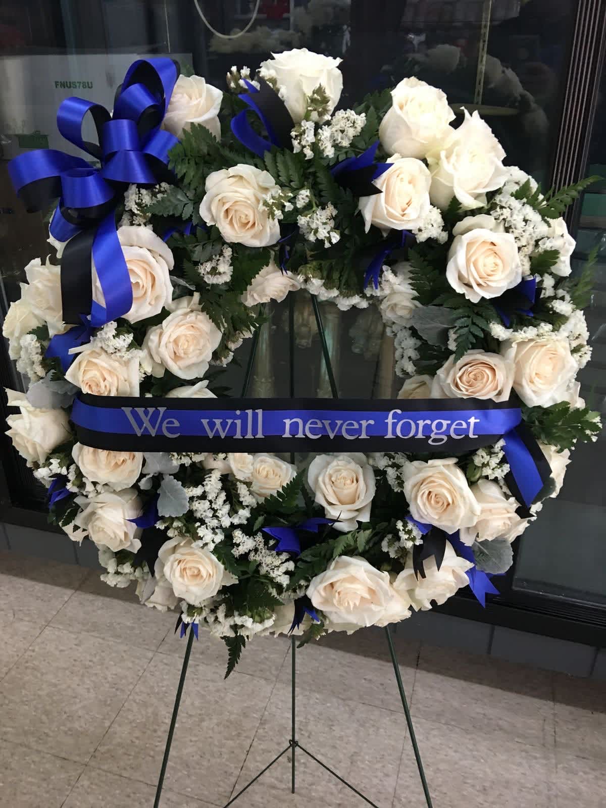 White rose funeral wreath with blue ribbon on an easel