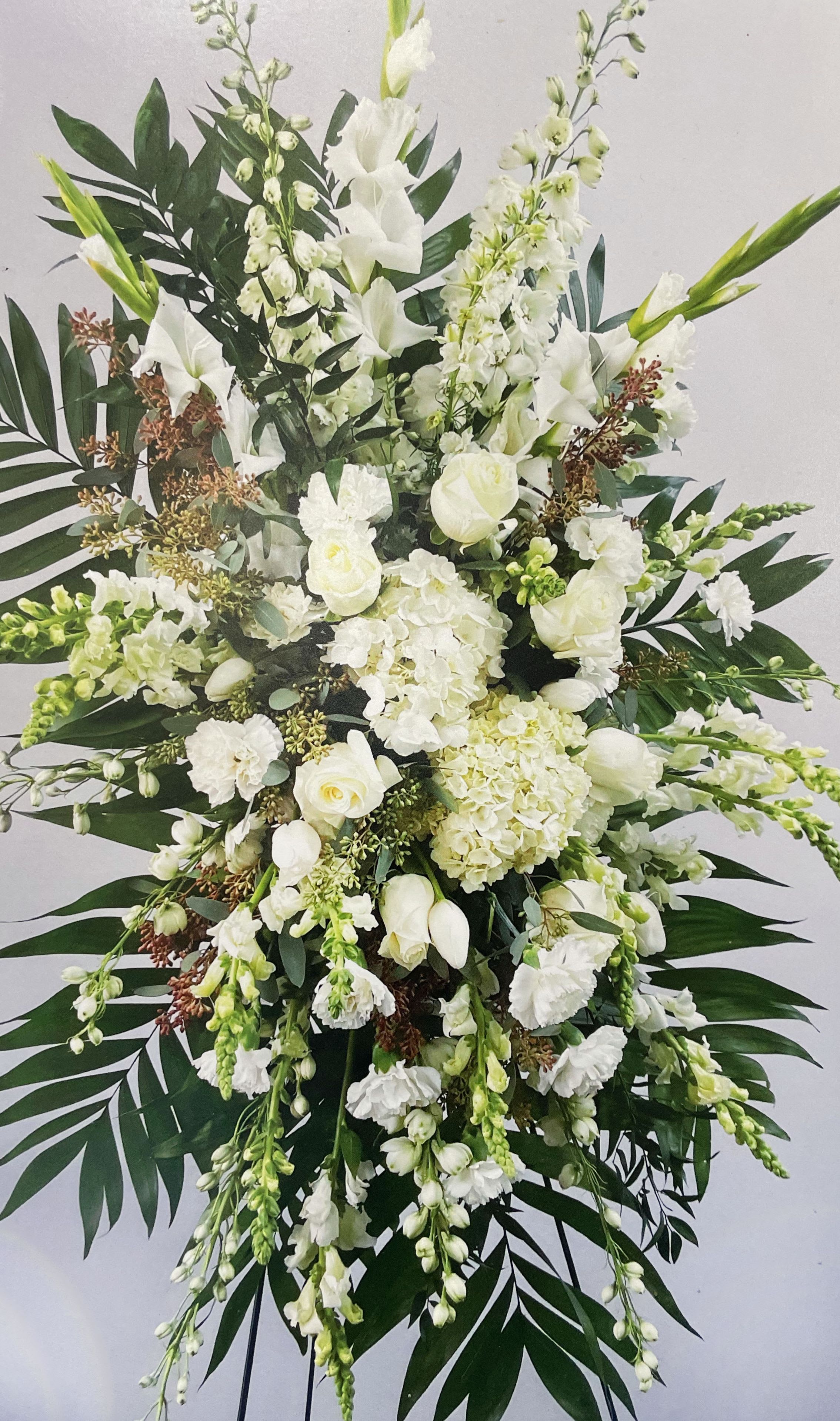 Large white floral standing spray with cascading blooms and dark palm leaves