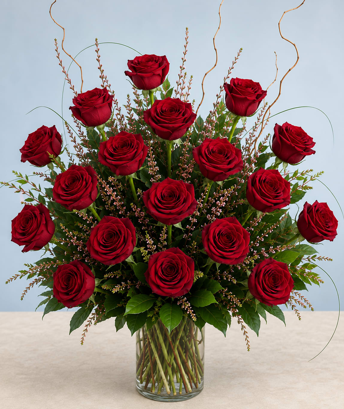 18 Red Roses - Deep red roses with lush green foliage and white accents, arranged upright in a clear glass vase-romantic, classic design perfect for any occasion.