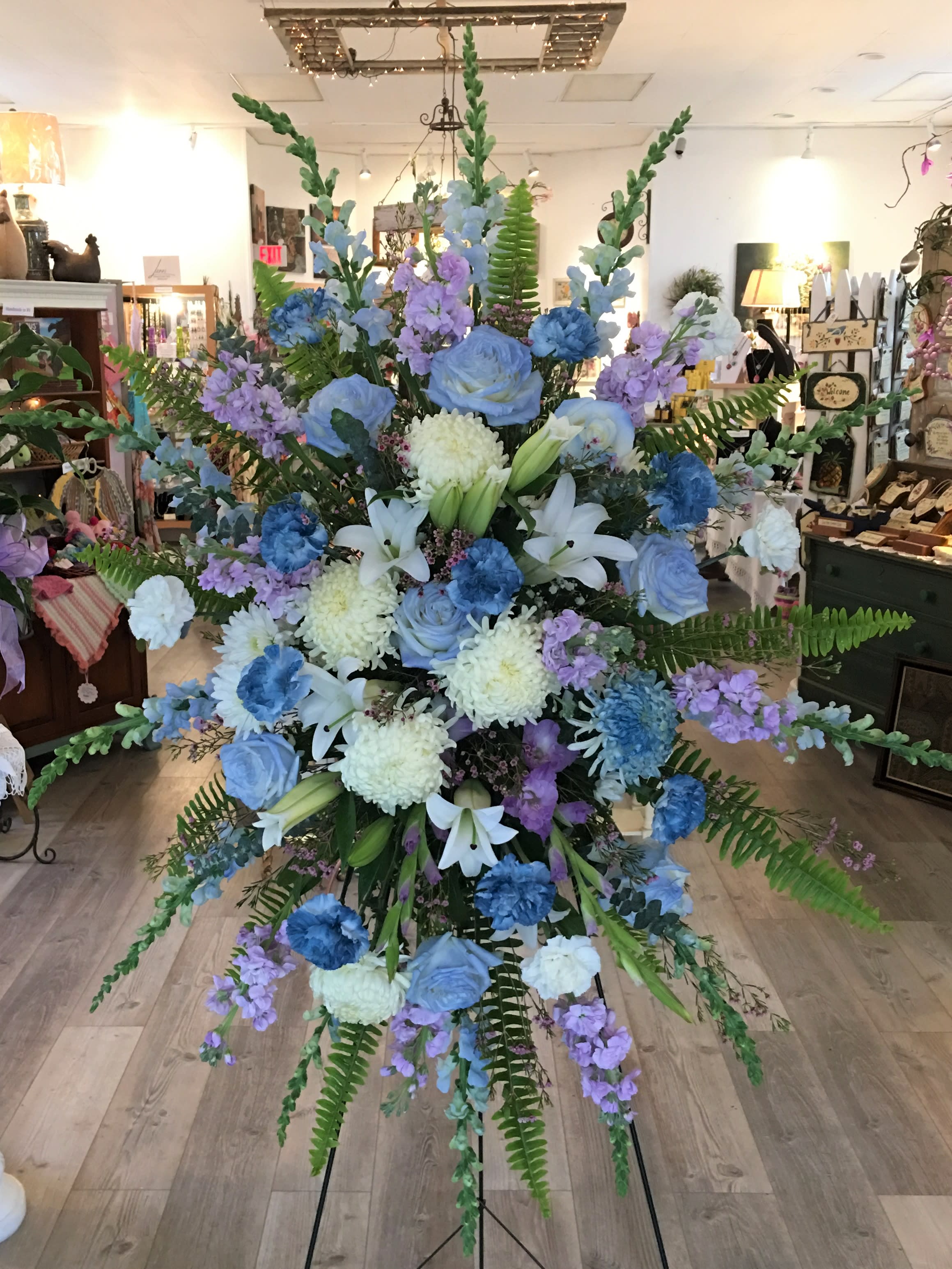 Lavender, Blue &amp; White Standing Spray Funeral Tribute by Petals - This elegant standing tribute features a premium selection of roses, lilies, snapdragons, and seasonal blooms. While specific flowers may vary slightly based on daily availability, we always maintain the arrangement's beautiful aesthetic.  For a custom color palette, please call us at 401-828-0701 for a personal consultation. 
