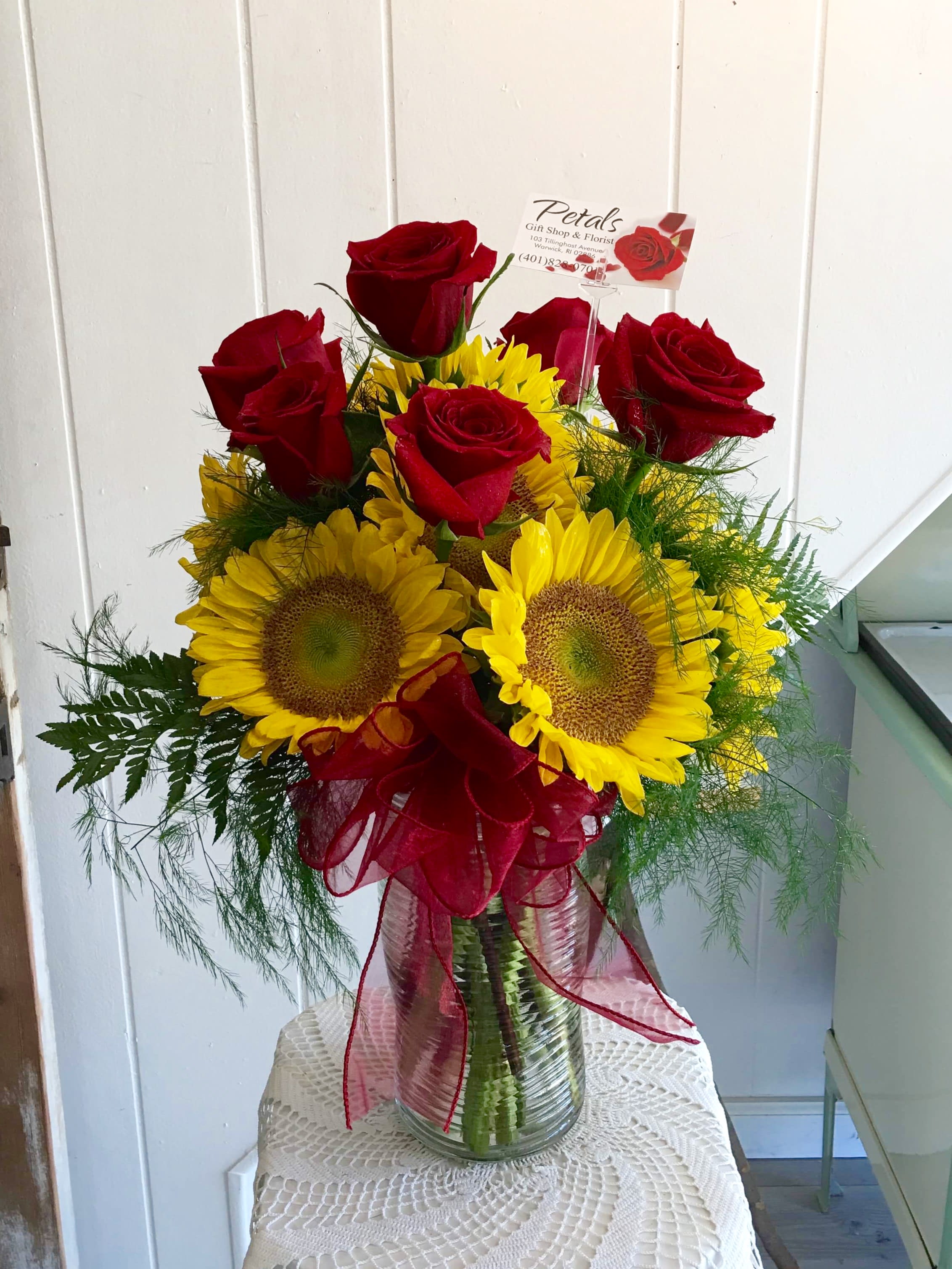 Radiant Sunflowers and Red Roses by Petals - "Radiant Sunflower &amp; Rose Arrangement" This stunning arrangement combines the cheerful beauty of bright yellow sunflowers with the classic elegance of a half-dozen premium red roses, all presented in a tall vase. Known for their joyous symbolism, sunflowers are sure to bring happiness to any recipient. Please note that sunflower sizes and colors may vary, with some having darker centers. For custom rose colors or other modifications, please get in touch with us at 401-828-0701.      