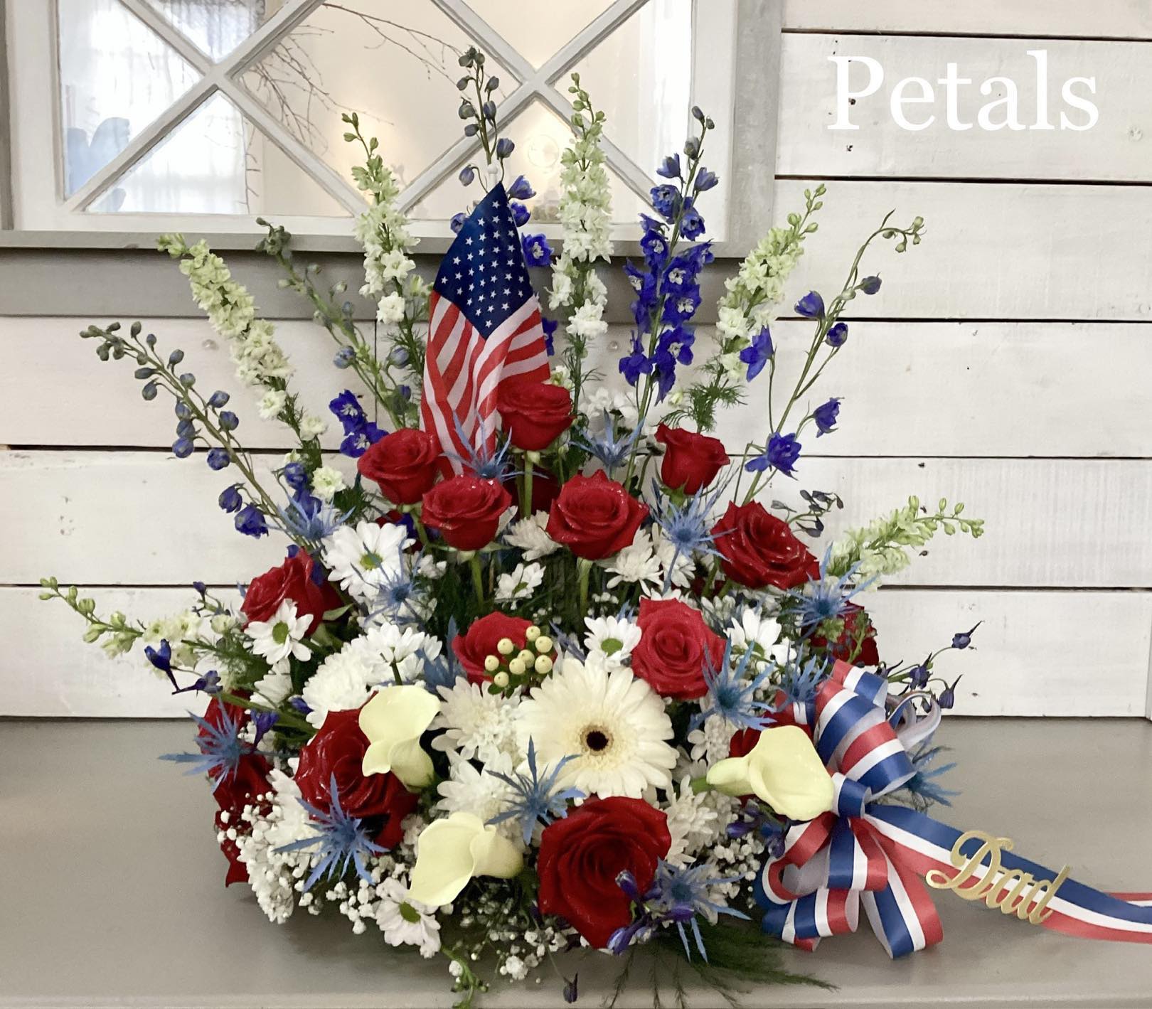Red roses and white flowers arranged with an American flag and ribbon