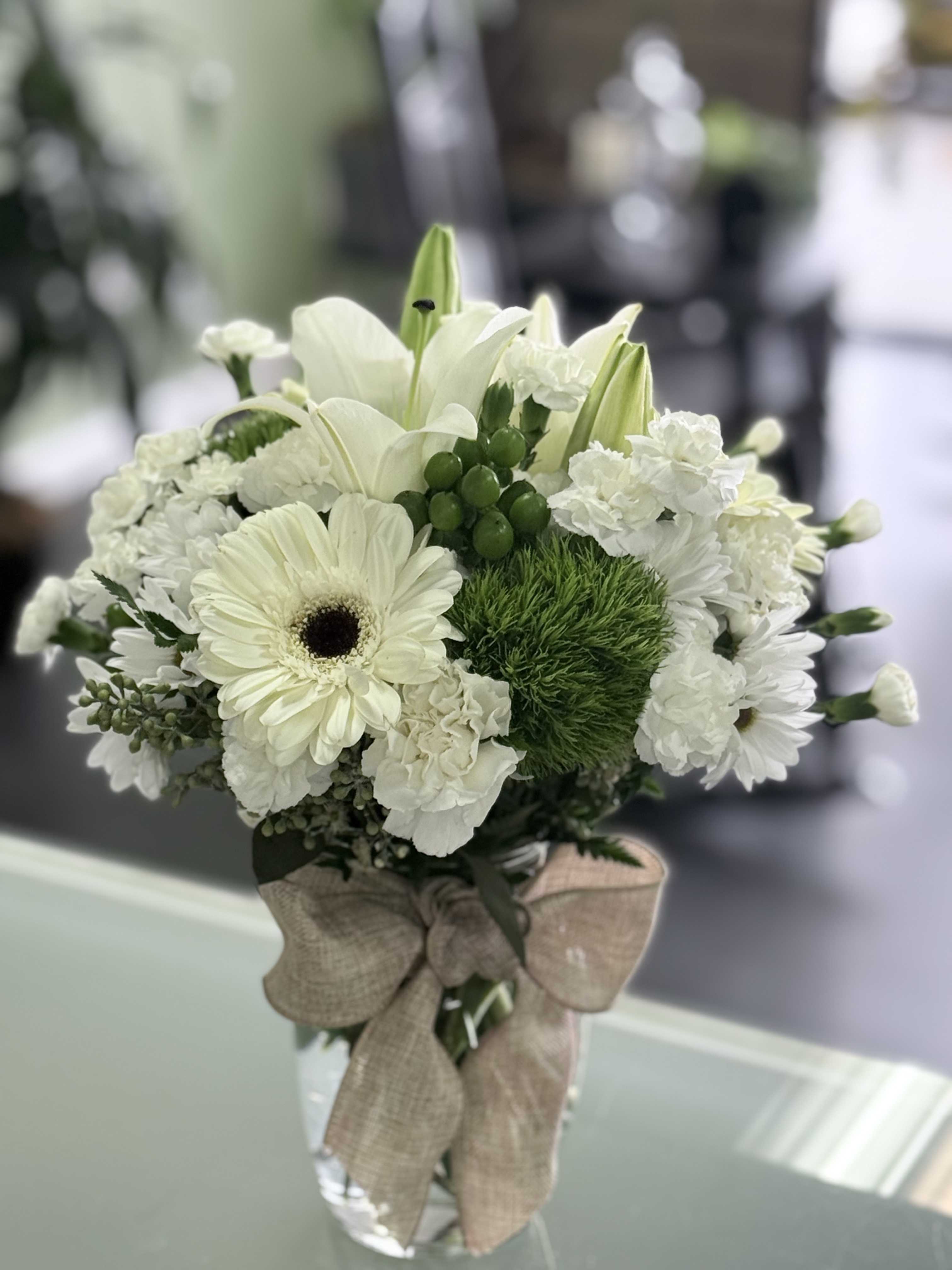 White floral bouquet in a clear glass vase with a burlap bow