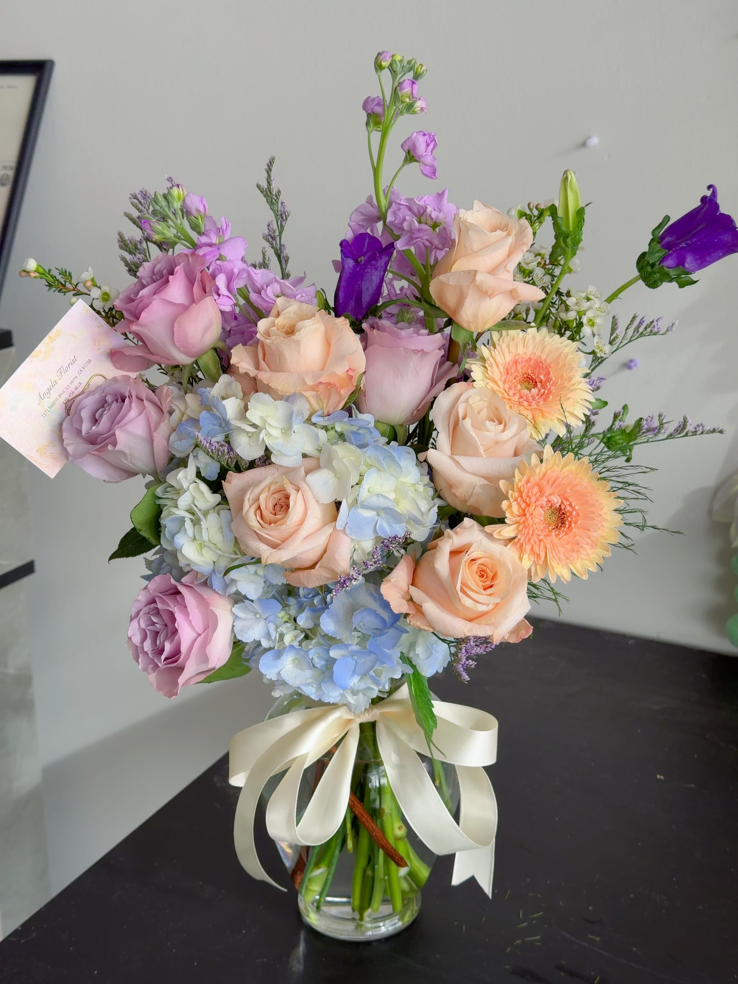 Bouquet of pastel roses, hydrangeas, and purple blooms in a glass vase