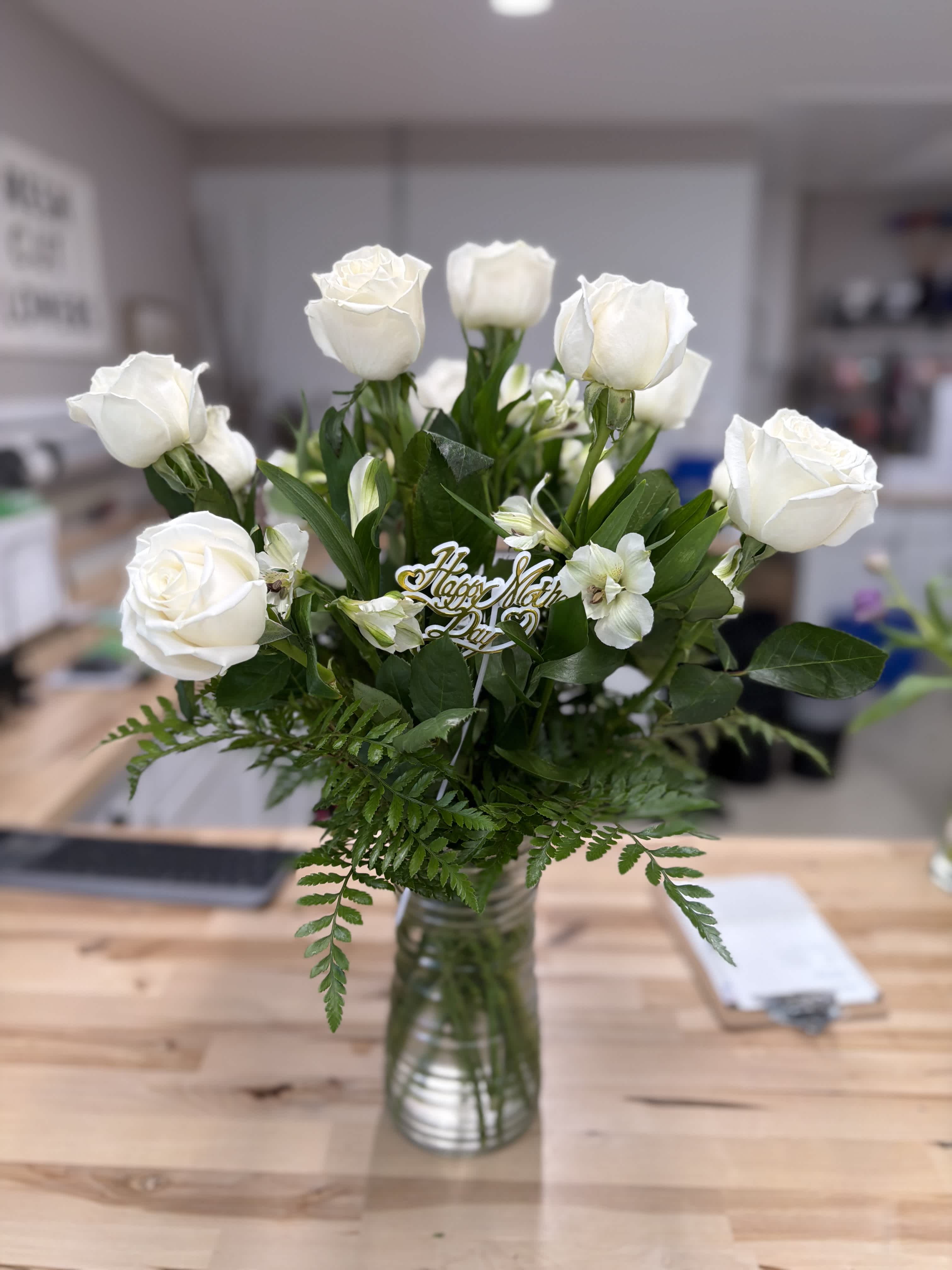 White roses and small white flowers in a glass vase with greenery