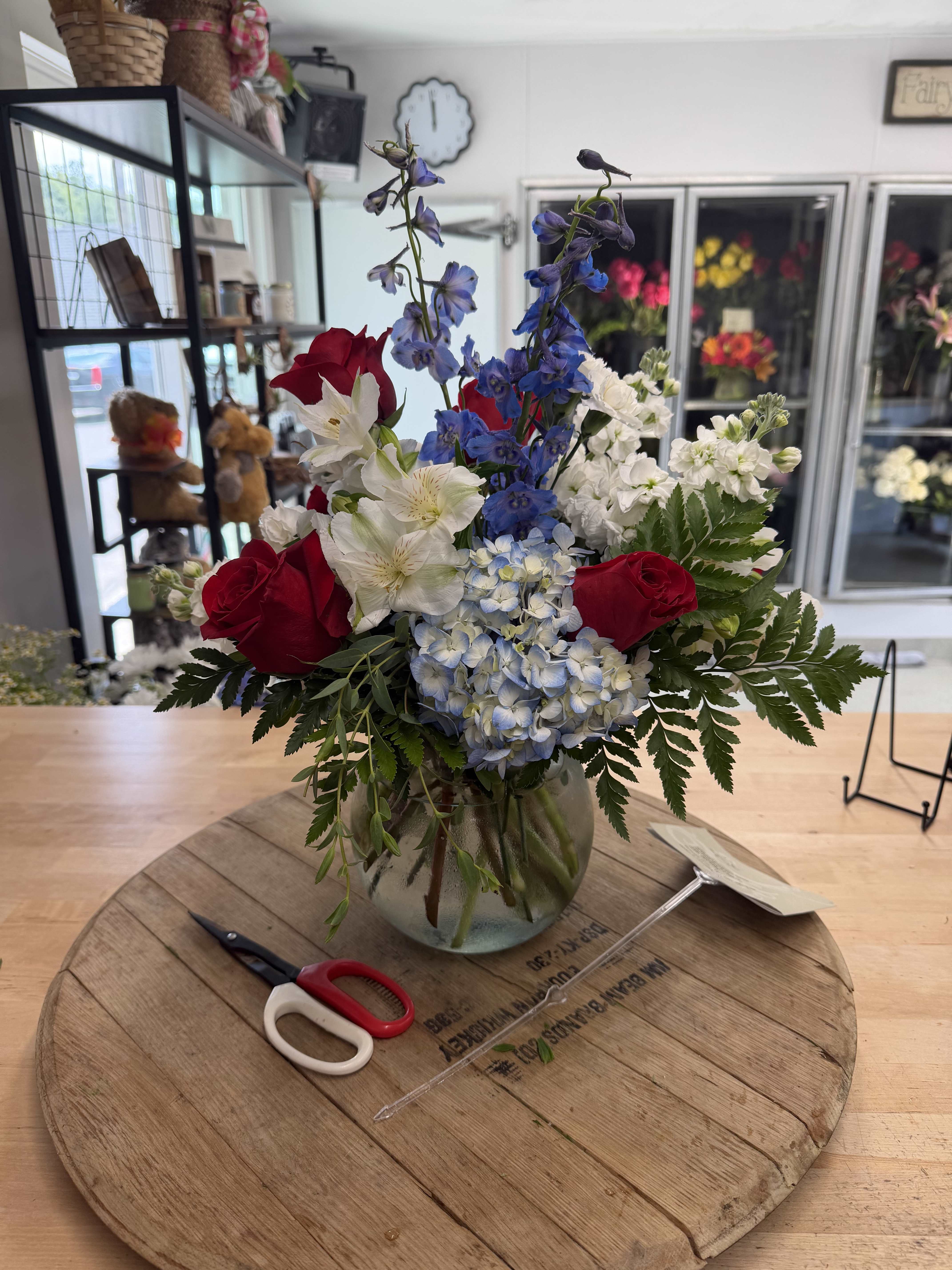 Mixed bouquet with red roses, blue delphinium, white alstroemeria, and hydrangea in a glass vase
