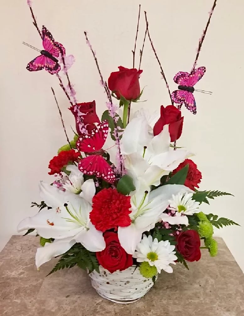 Red roses and white lilies in a white basket with pink butterfly picks