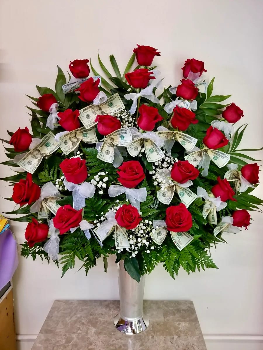 Red roses arranged in a tall vase with dollar bills and white bows