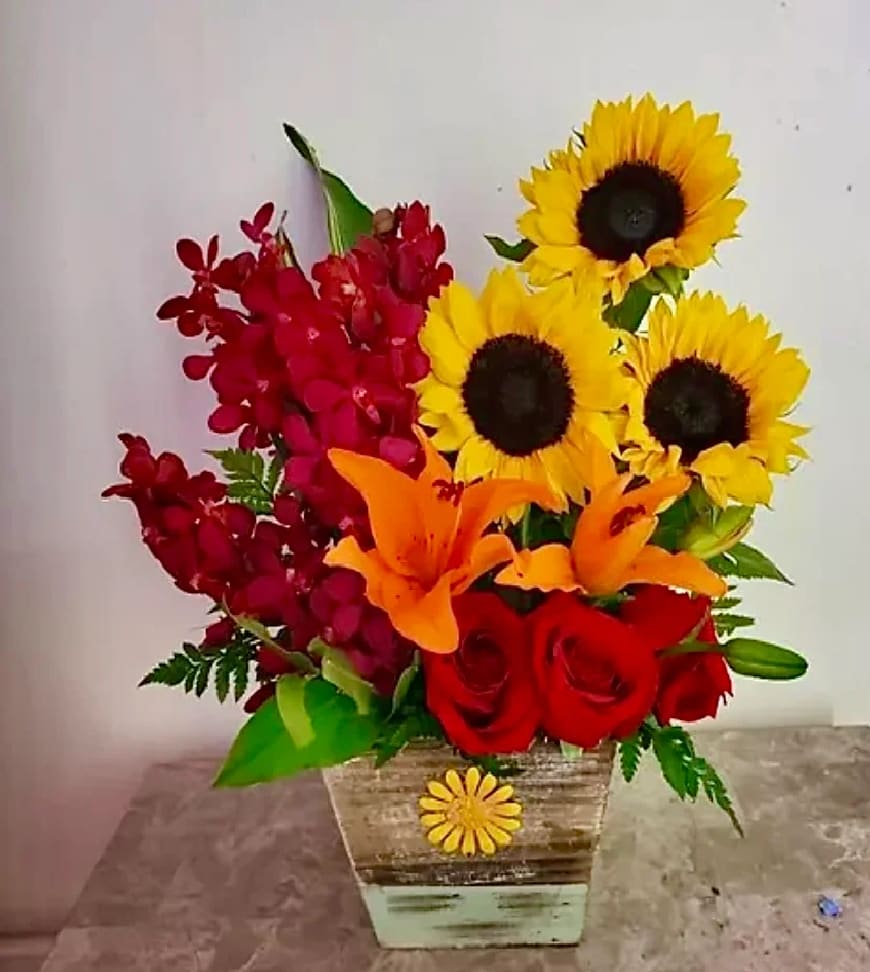 Bouquet of sunflowers, red roses, orange lilies, and red orchids in a wooden container