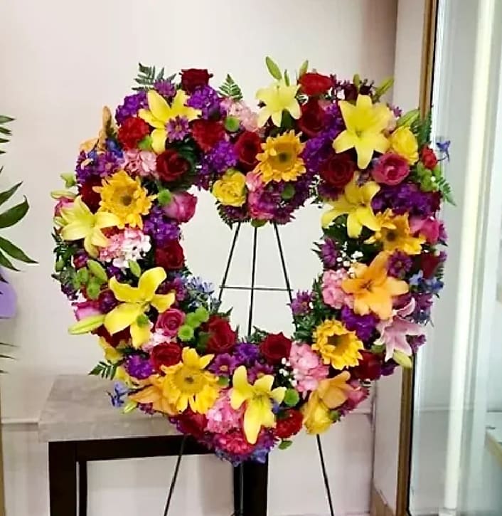 Heart-shaped floral wreath on a stand with yellow lilies and red roses