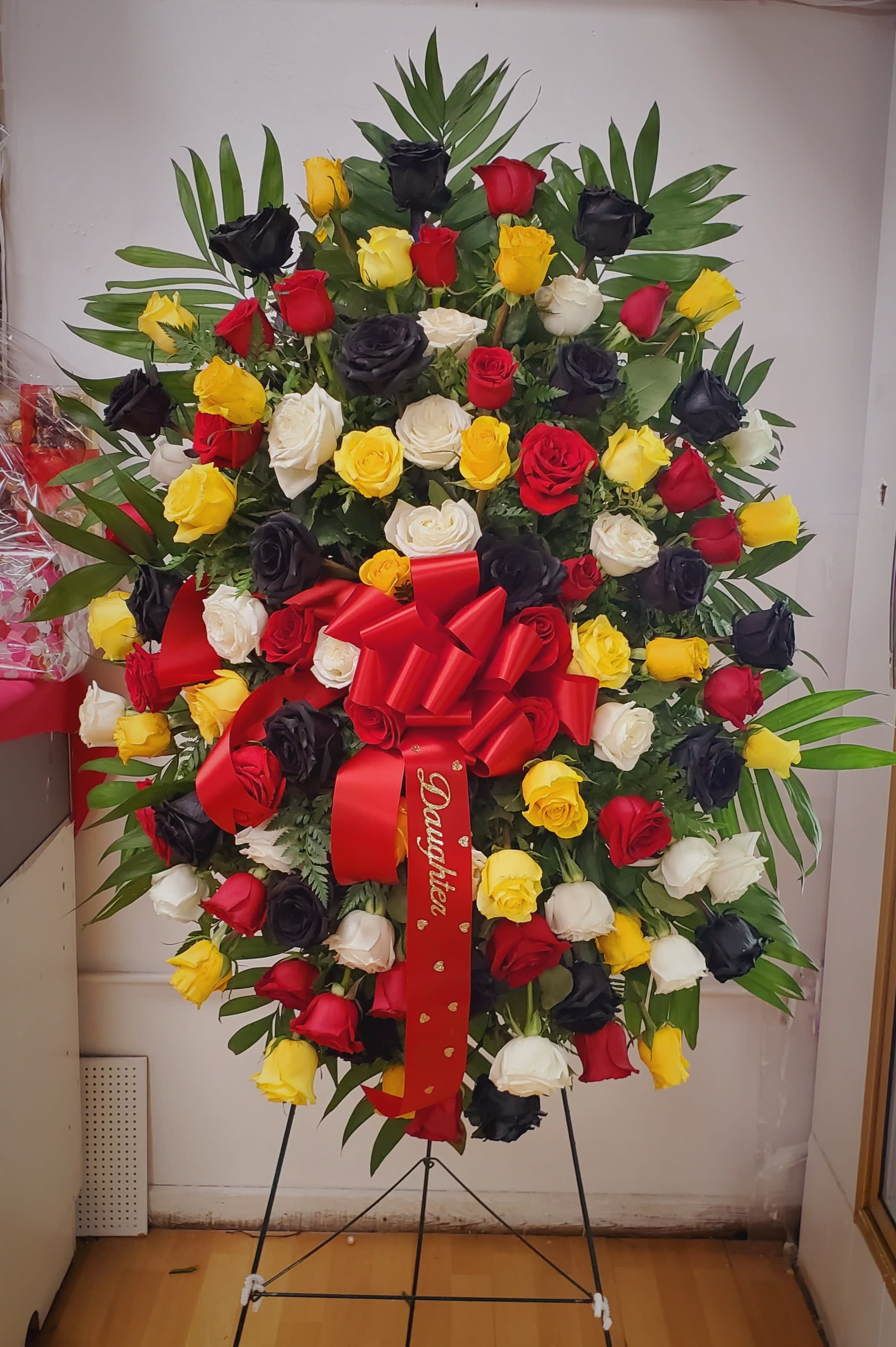 Large standing rose arrangement in red, yellow, white, and black with a red bow