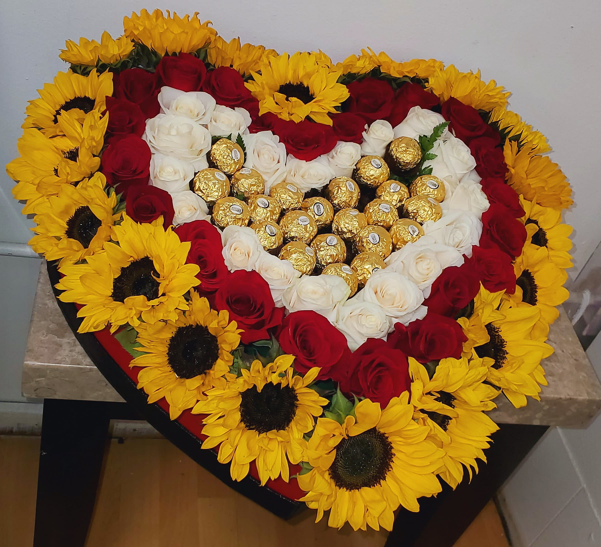 Heart-shaped arrangement of red and white roses with sunflowers and gold chocolates