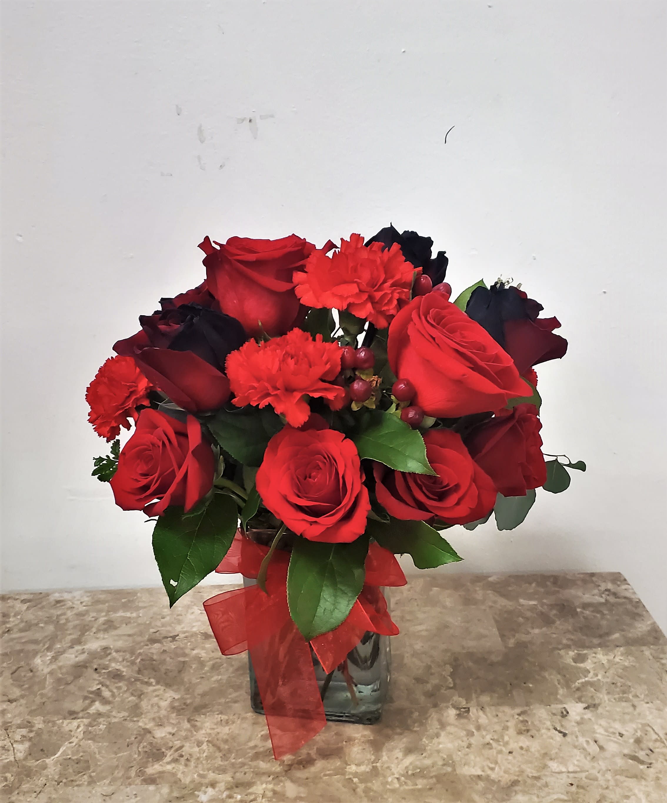 Red roses and carnations arranged in a glass vase with a red ribbon.