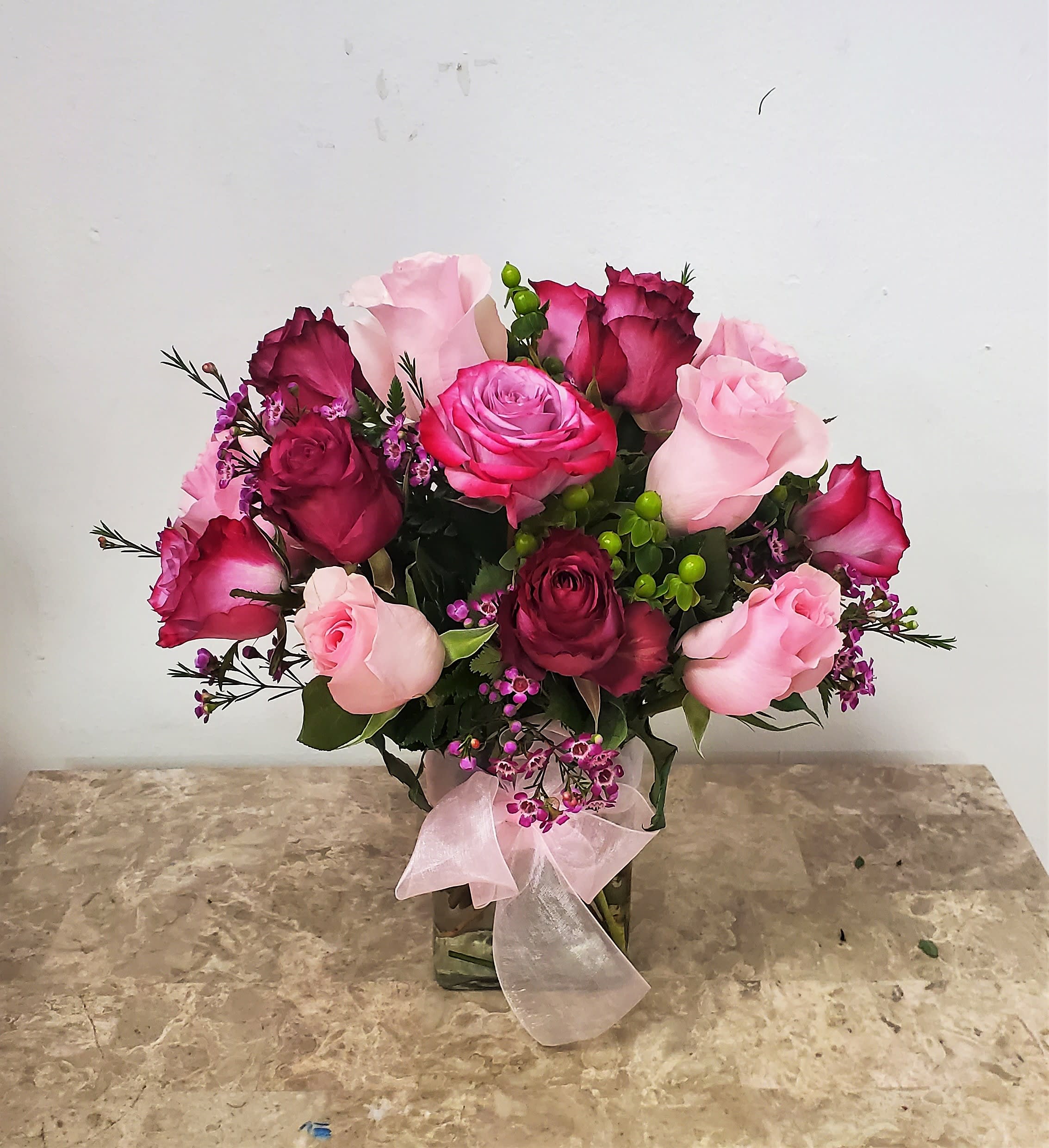 Pink and burgundy roses in a glass vase with a pink ribbon