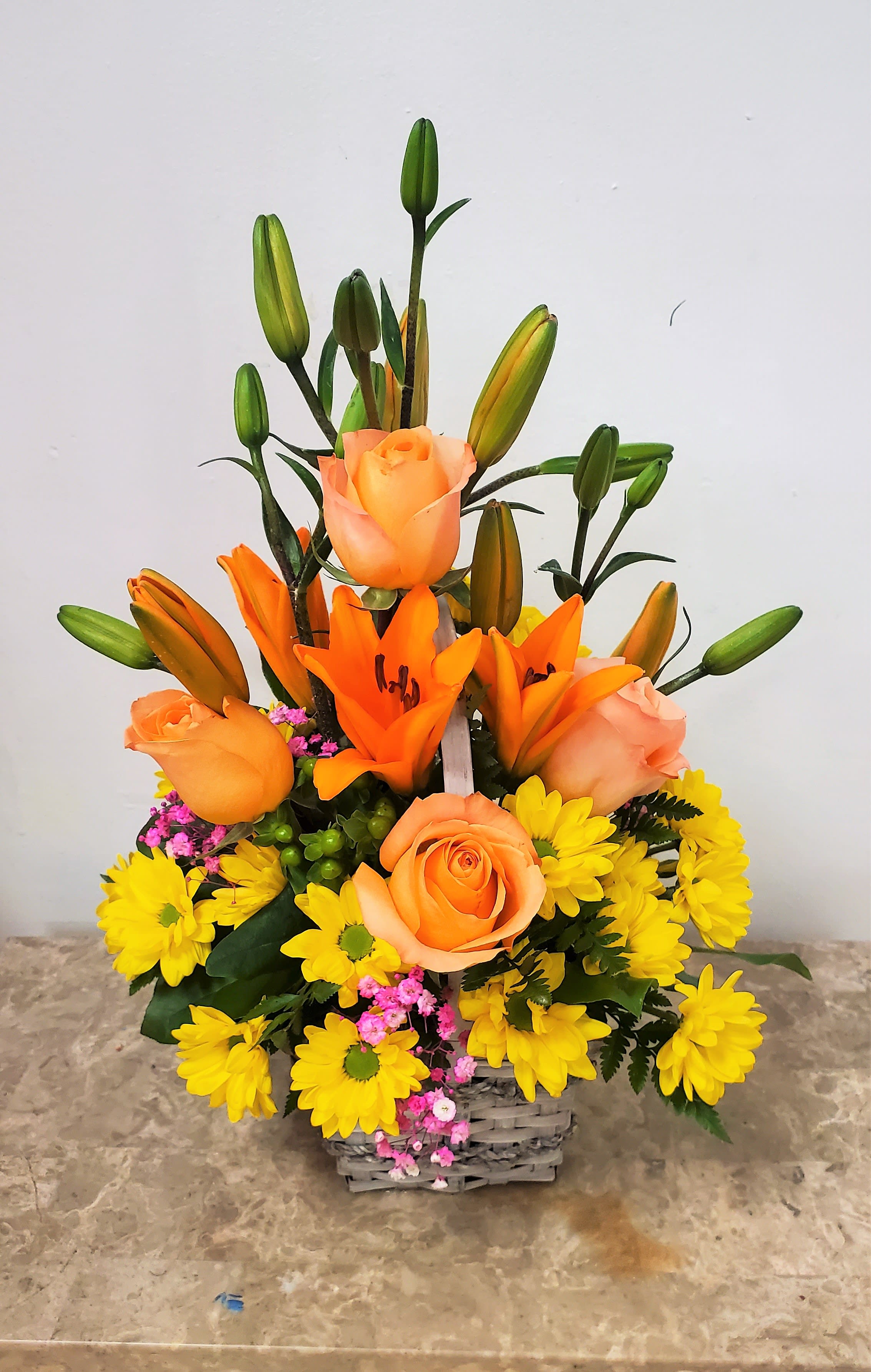 Orange roses and lilies in a basket with yellow daisies