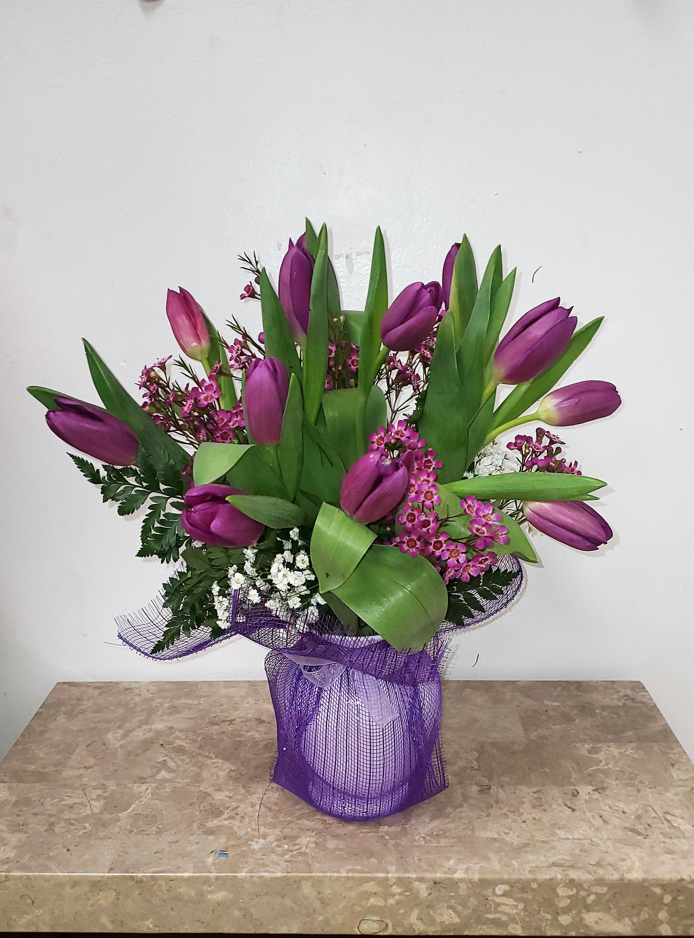 Purple tulips arranged in a wrapped bouquet with green foliage