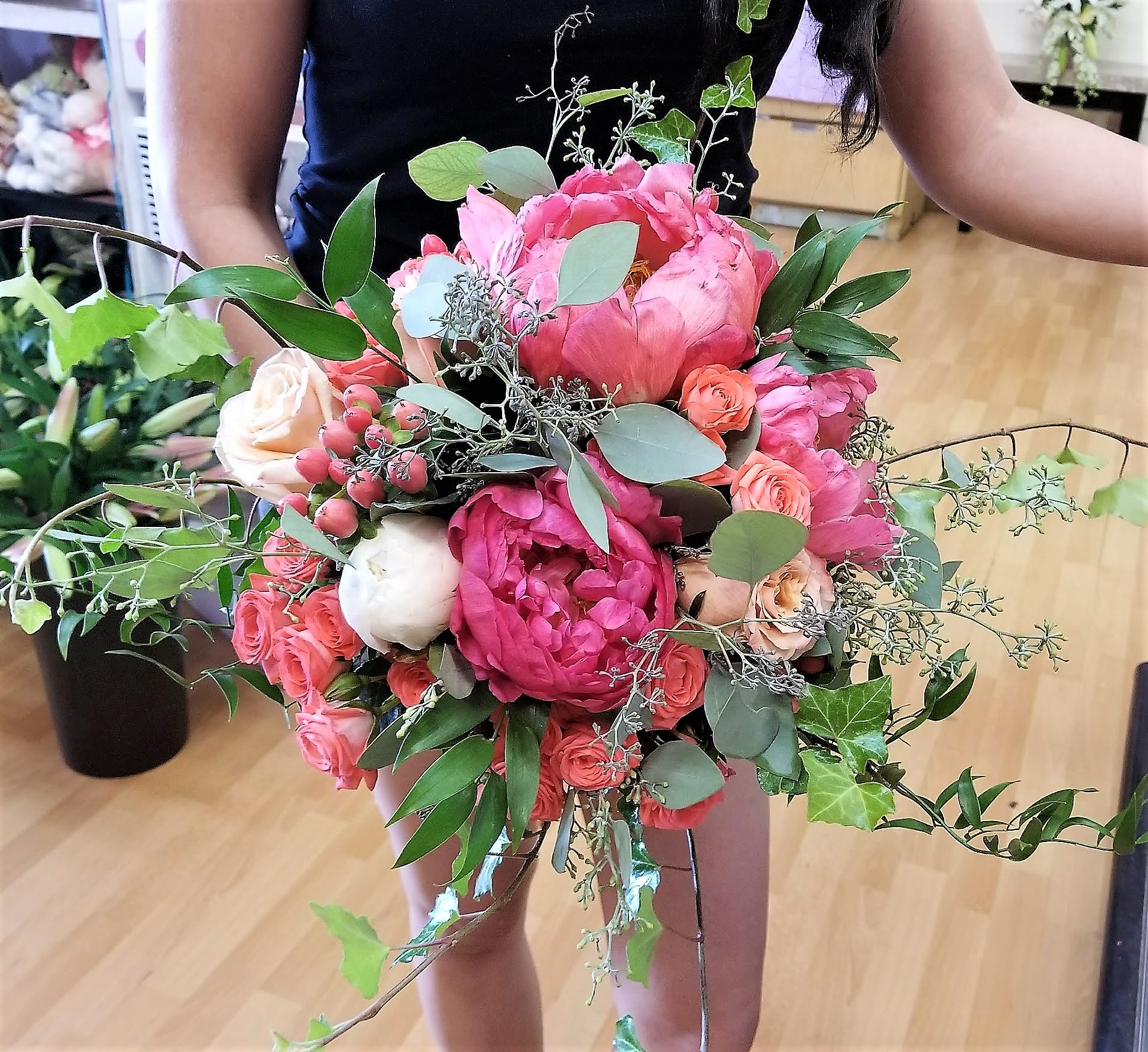 Handheld bouquet of pink peonies and roses with greenery