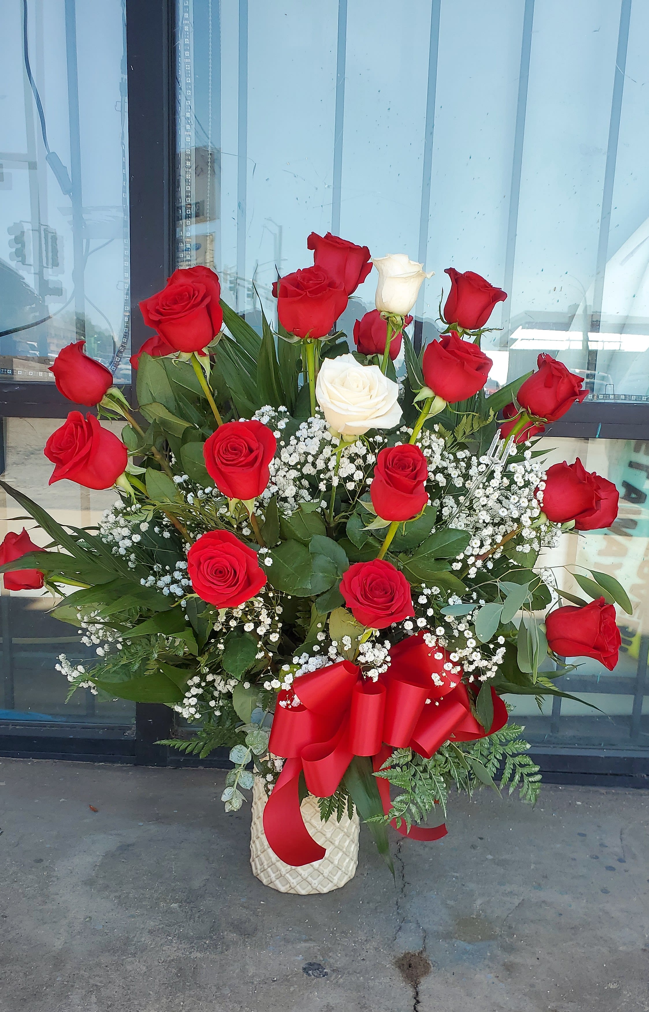 Tall bouquet of red and white roses in a cream vase with a red ribbon