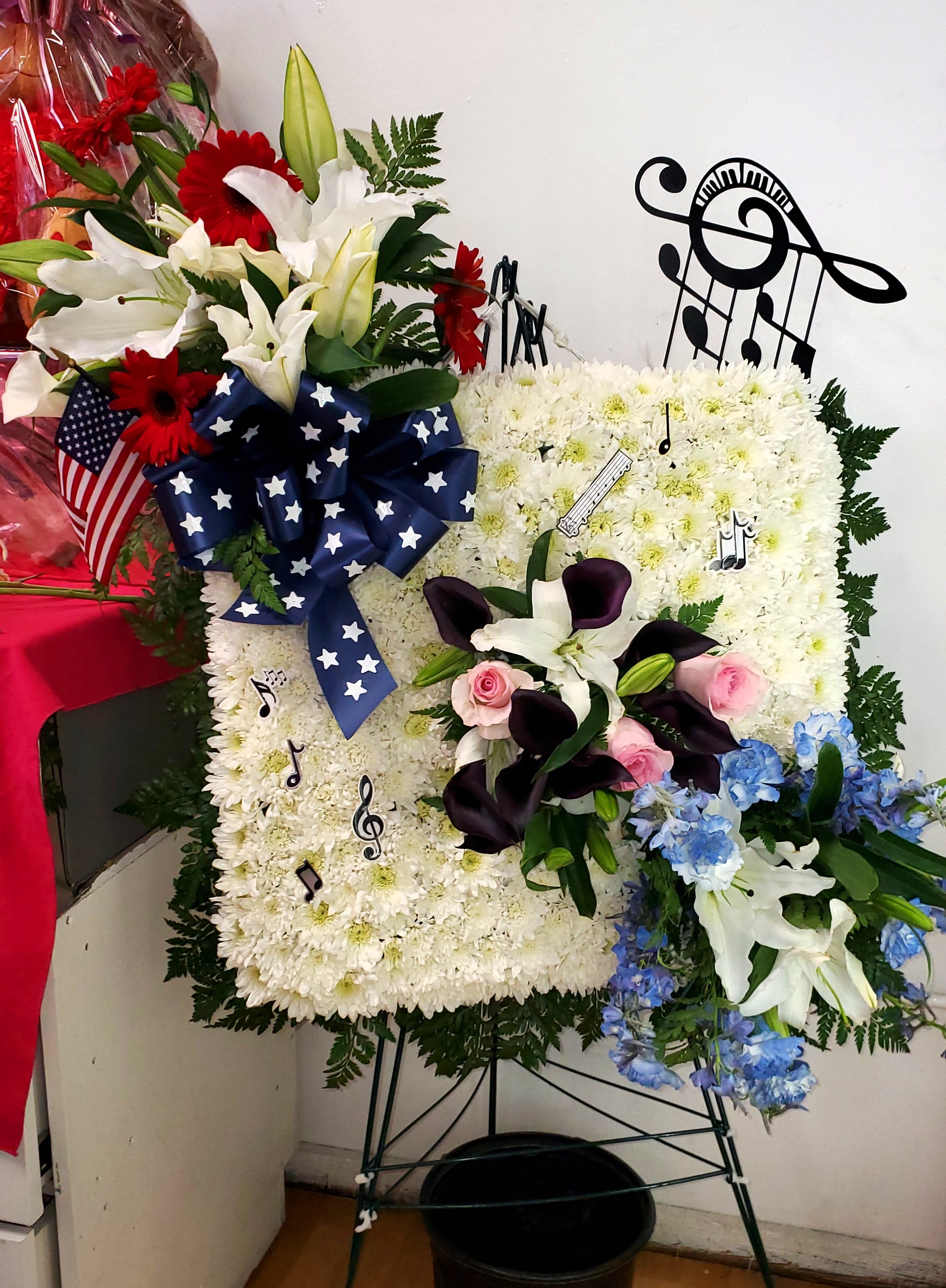 Floral standing spray with white lilies, red gerberas, and blue flowers on an easel
