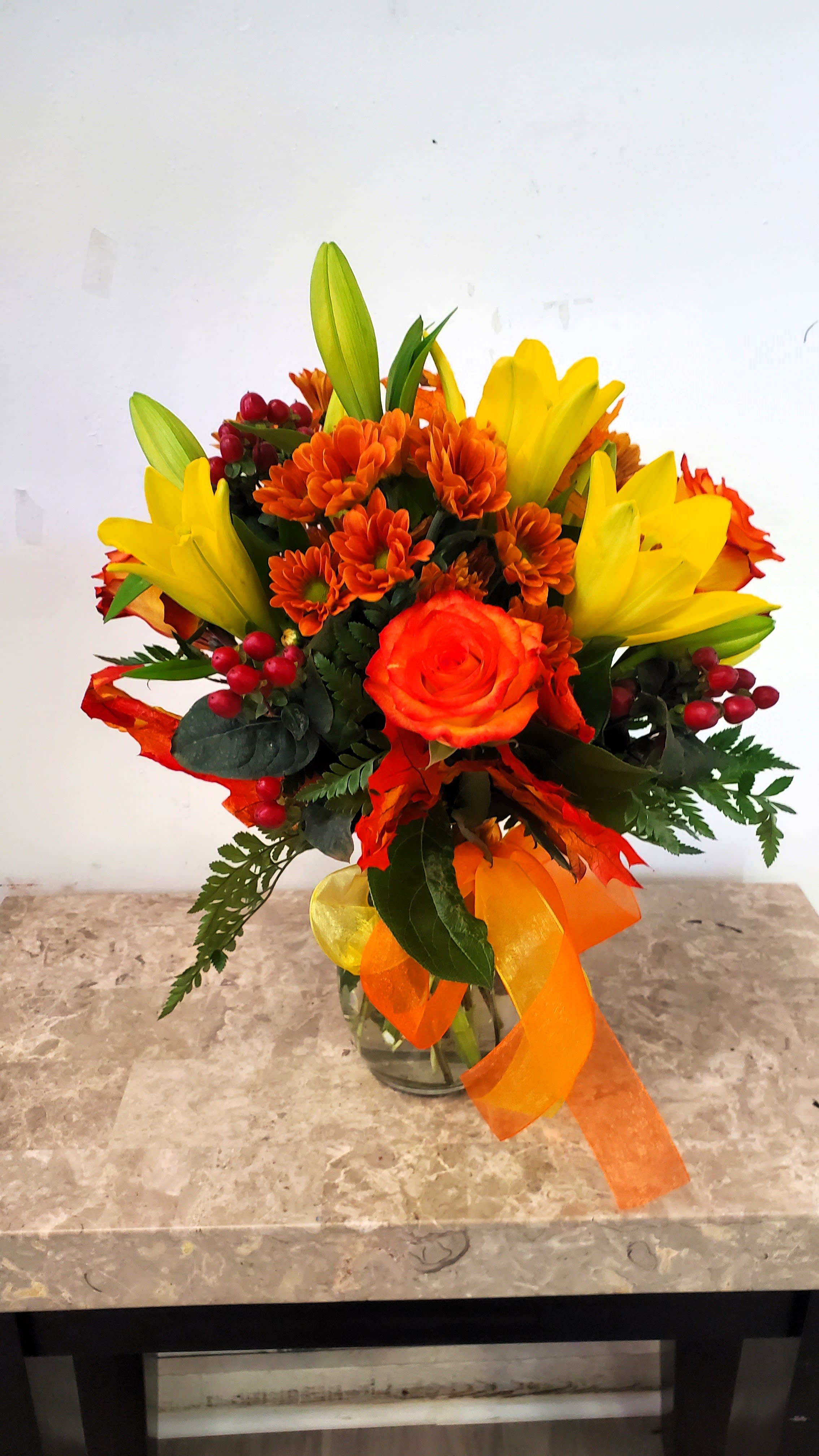 Orange and yellow bouquet in a glass vase with ribbon