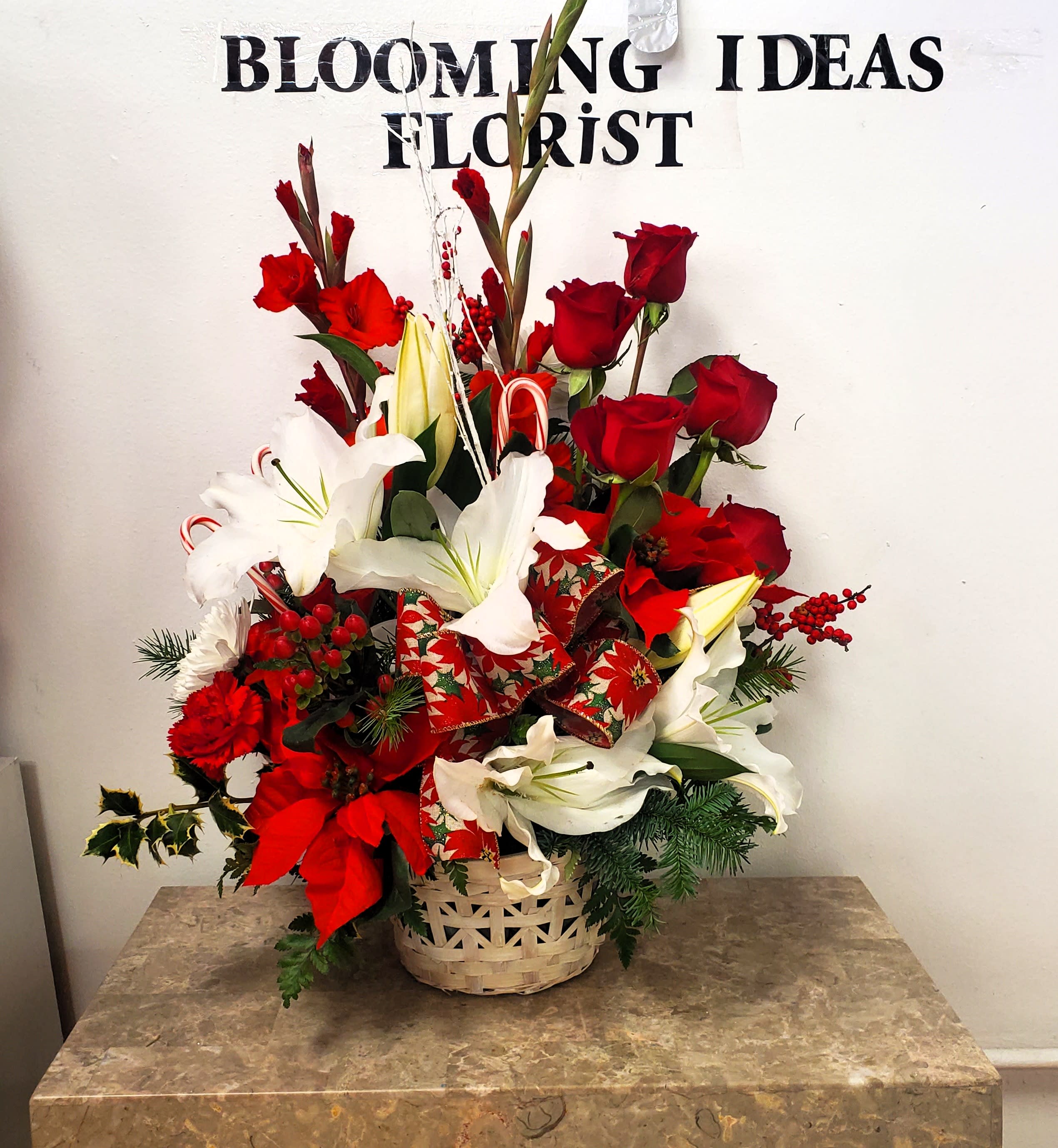 Red roses and white lilies arranged in a basket with holiday ribbon.