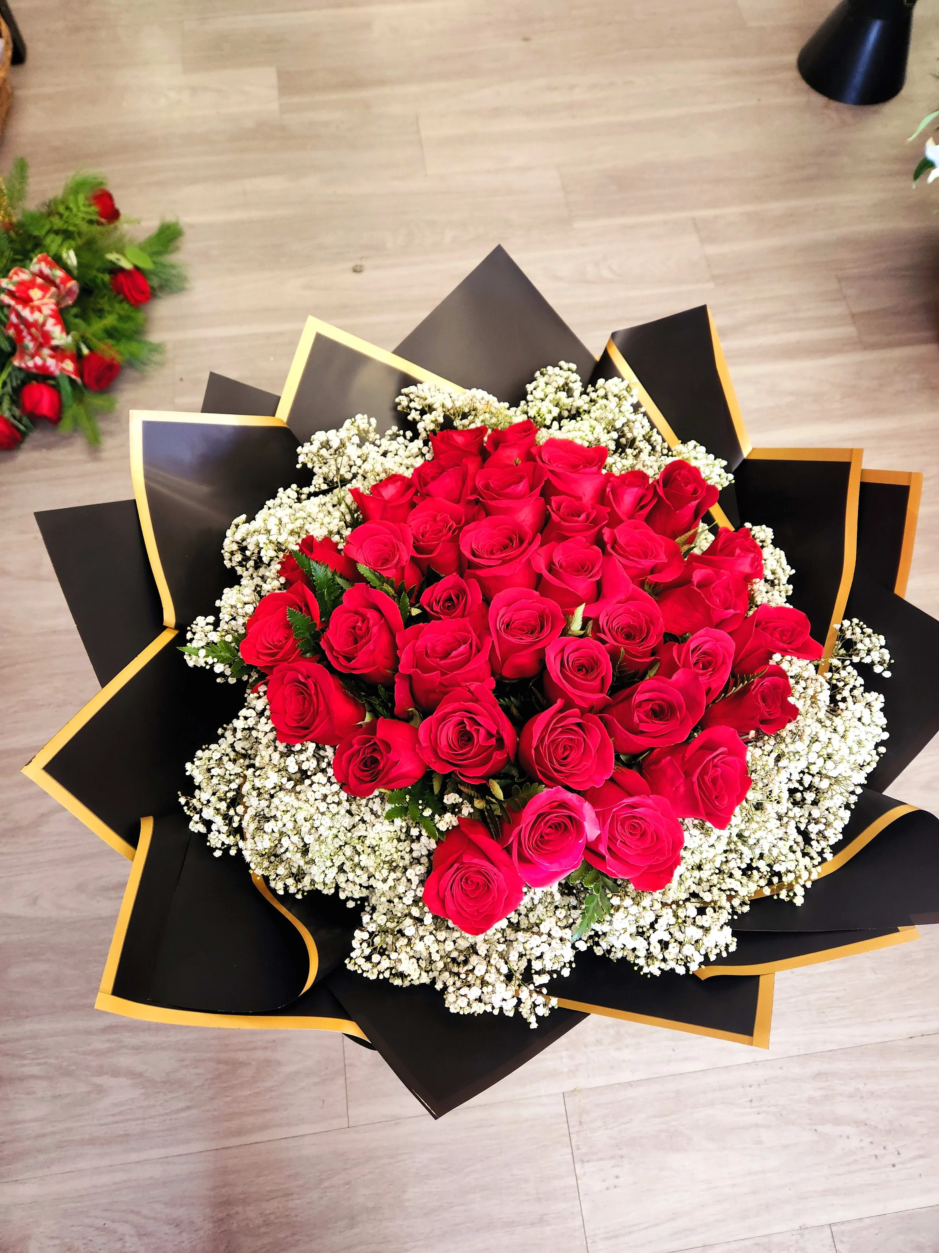 Large bouquet of red roses with white baby's breath in black and gold wrap
