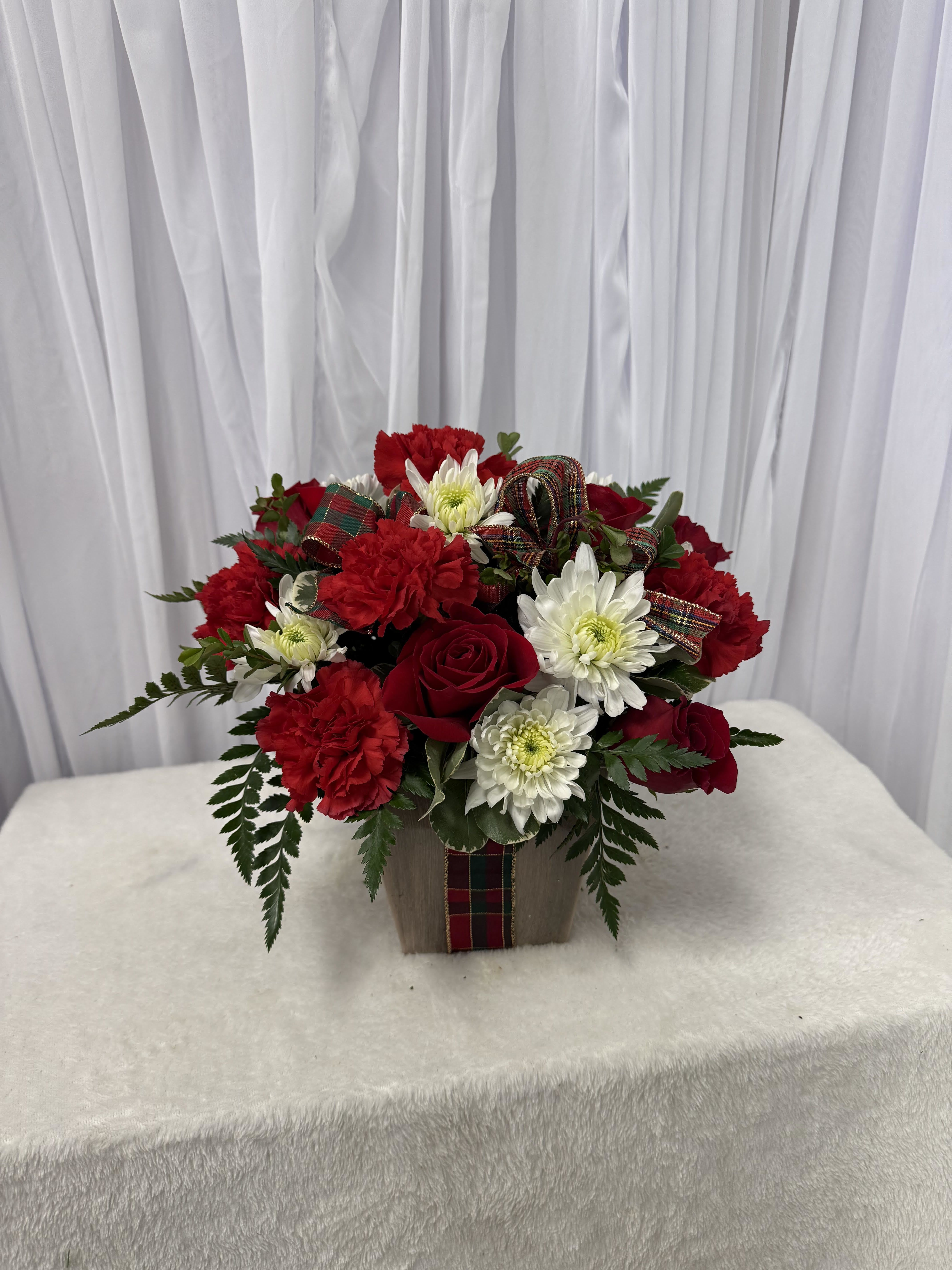 Red roses and white daisies in a square container with plaid ribbon