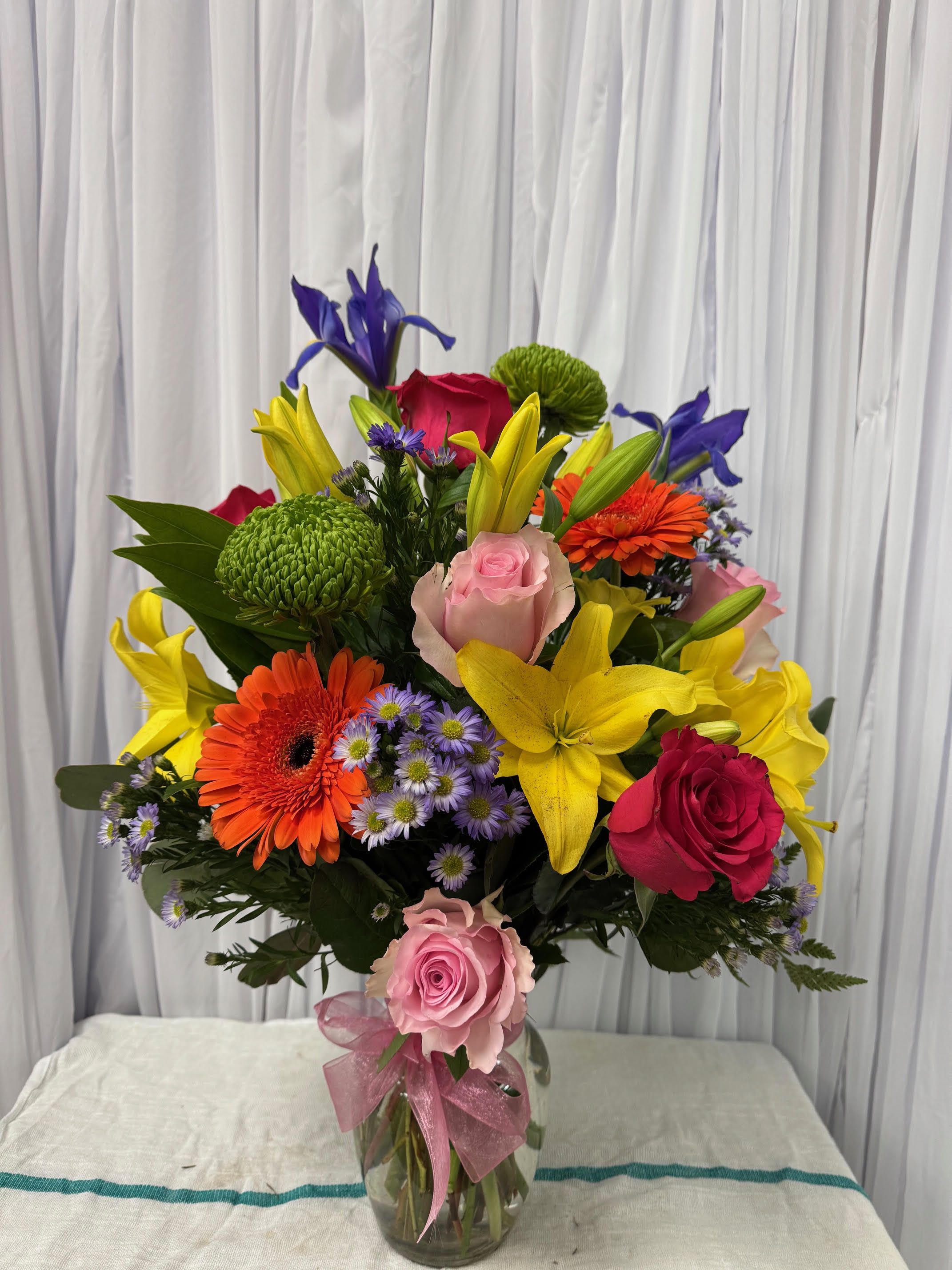 Colorful mixed bouquet in a glass vase with roses, lilies, and gerbera daisies