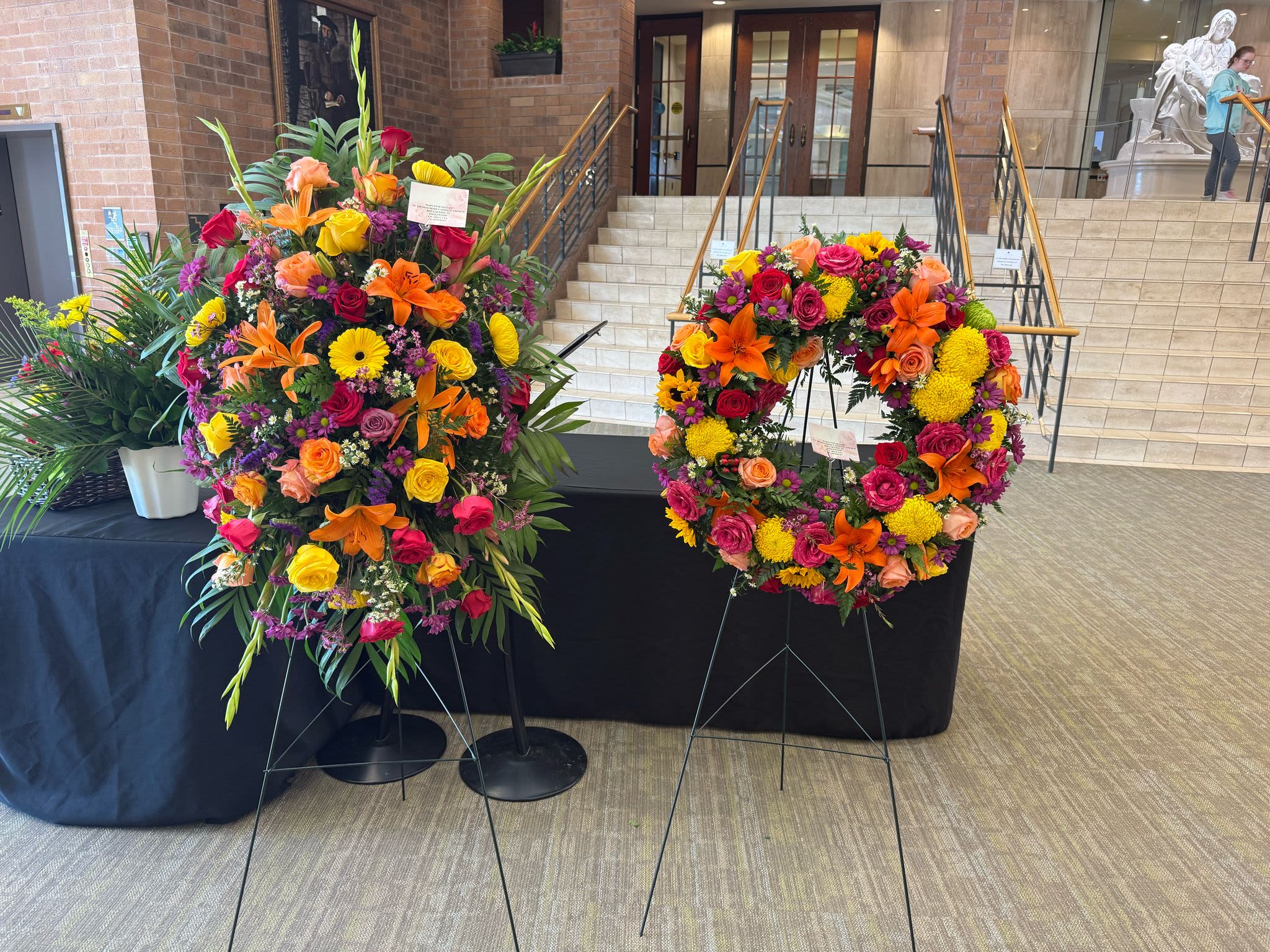 Two large floral wreaths on stands with bright mixed flowers