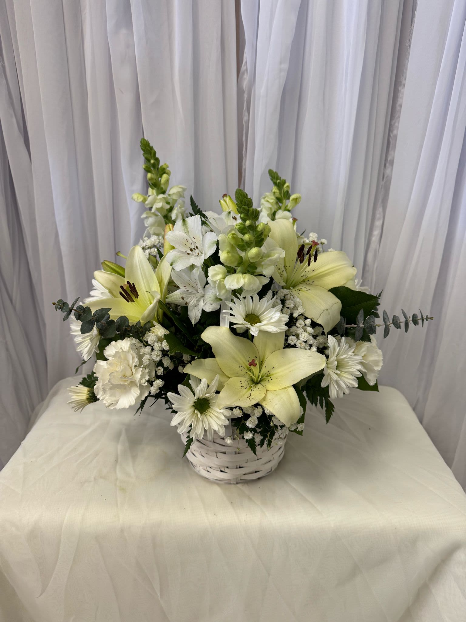 White lilies and daisies arranged in a white basket