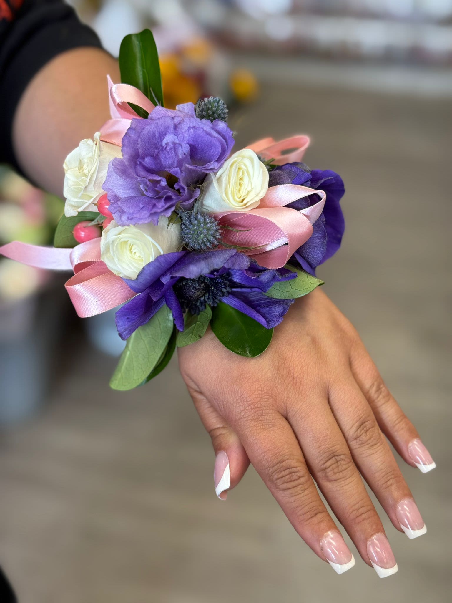 Purple and white wrist corsage with pink ribbon on a hand