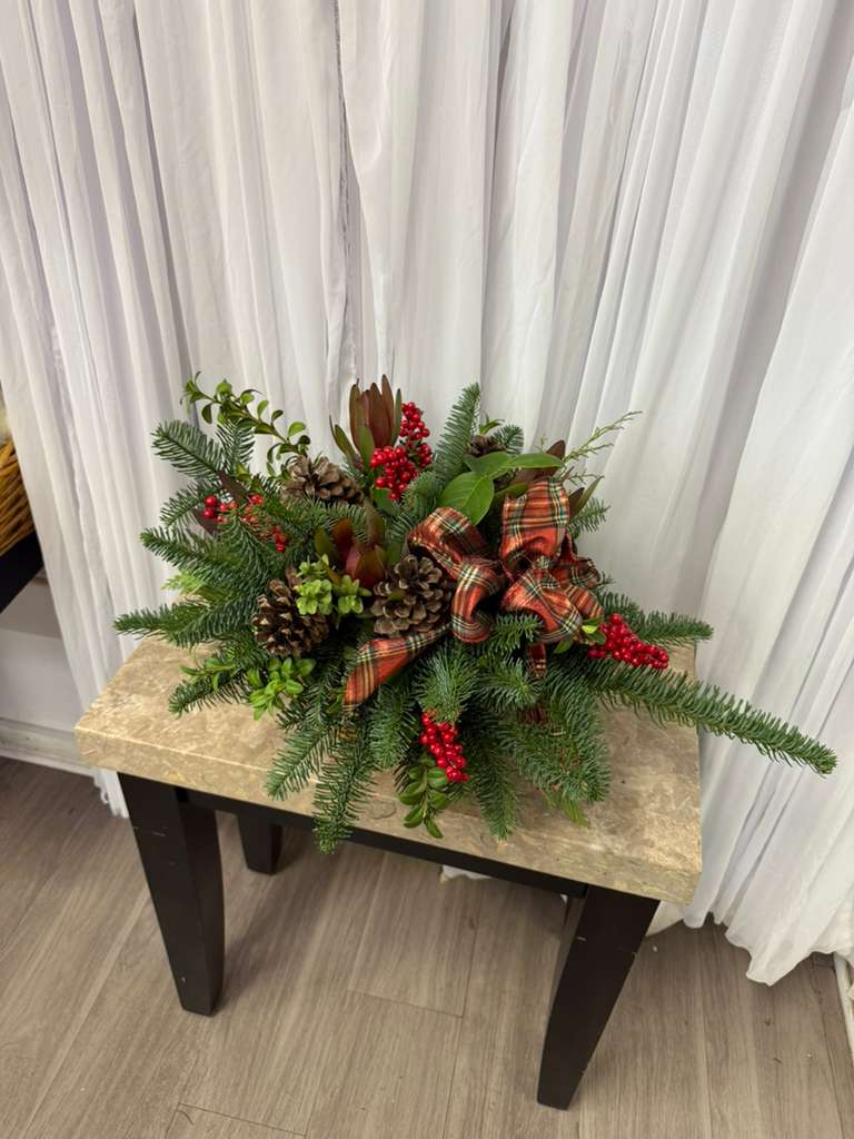 Holiday centerpiece with evergreen branches, pinecones, red berries, and a plaid bow