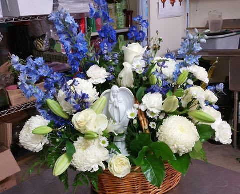 White and blue floral arrangement in a wicker basket with a small angel figurine