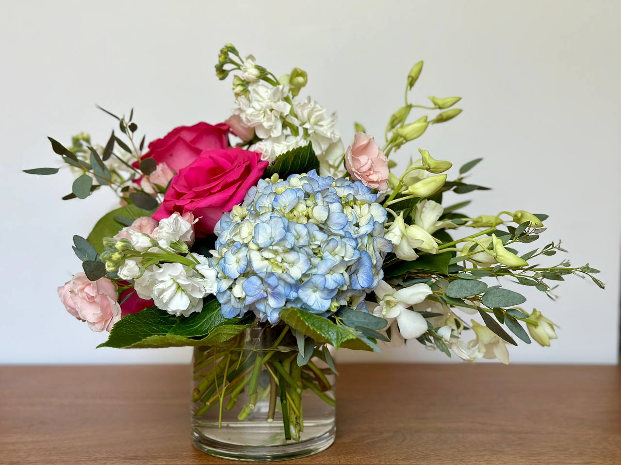 Mixed bouquet with pink roses, blue hydrangea, and white flowers in a glass vase