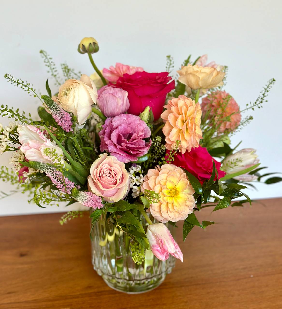 Mixed bouquet of pink, peach, and red flowers in a clear glass vase