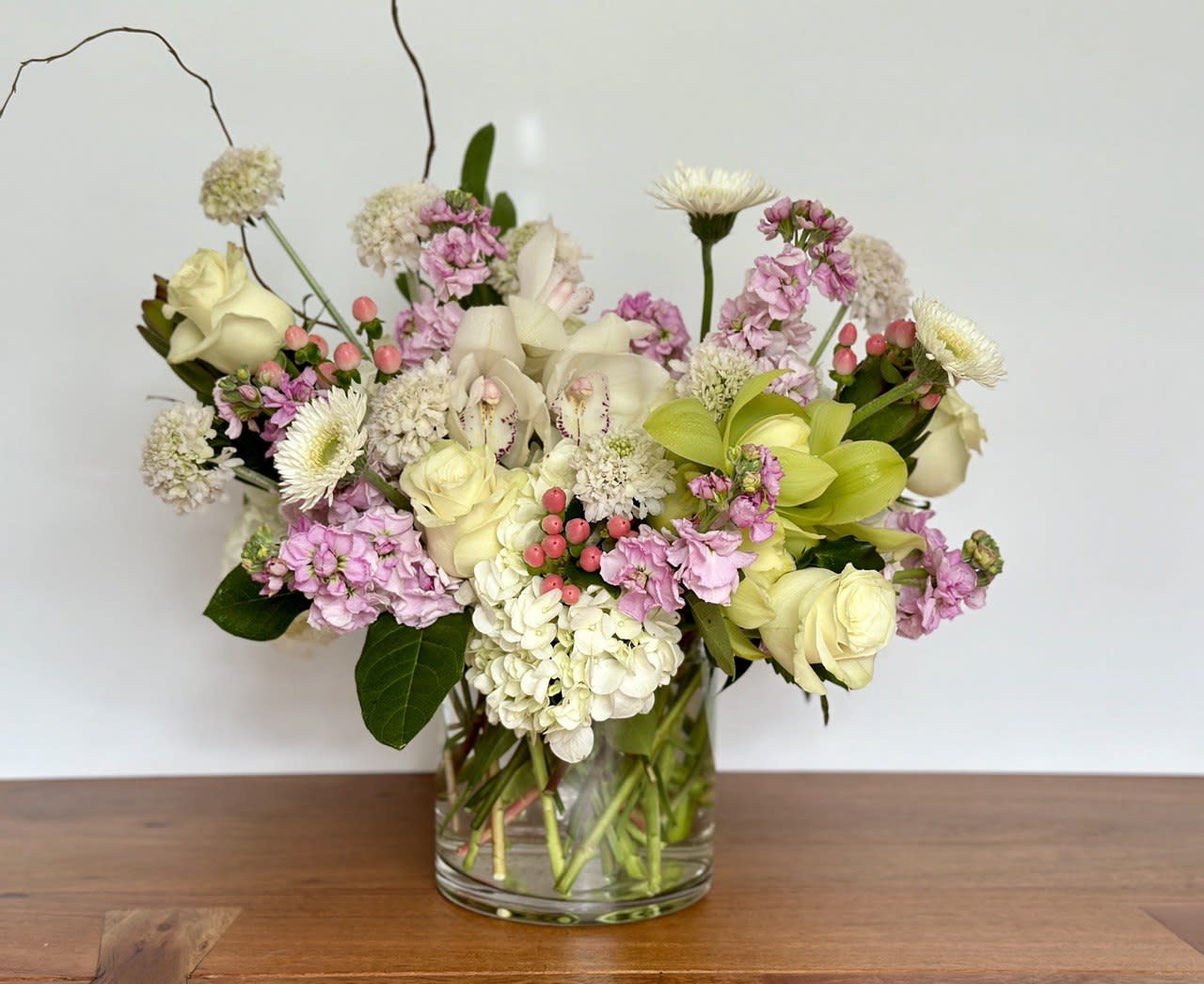Mixed bouquet of cream, pink, and green flowers in a clear glass vase