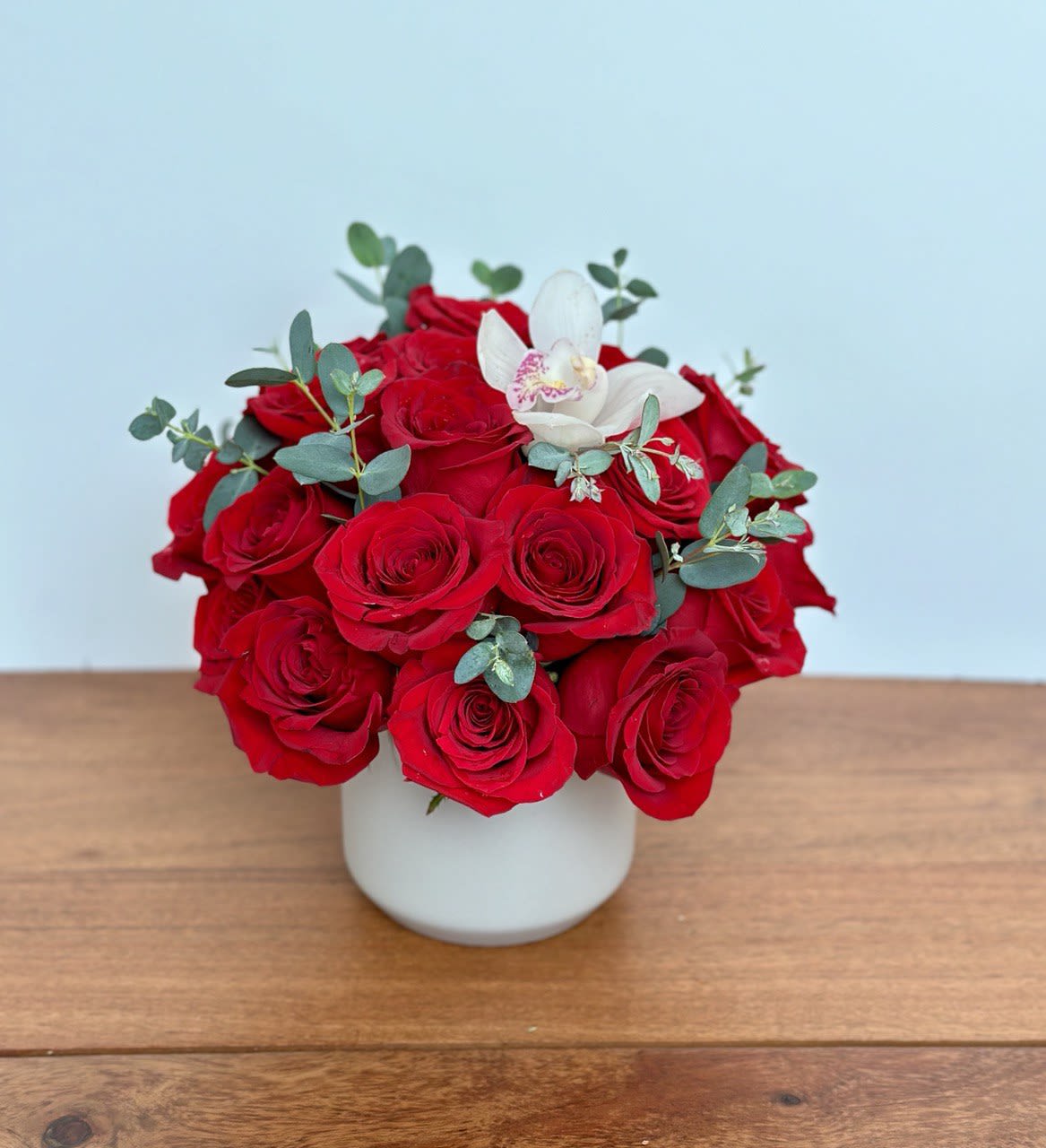 Red roses in a white vase with a white orchid bloom
