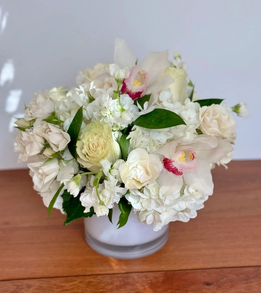 White floral arrangement in a round vase with pale roses and orchids