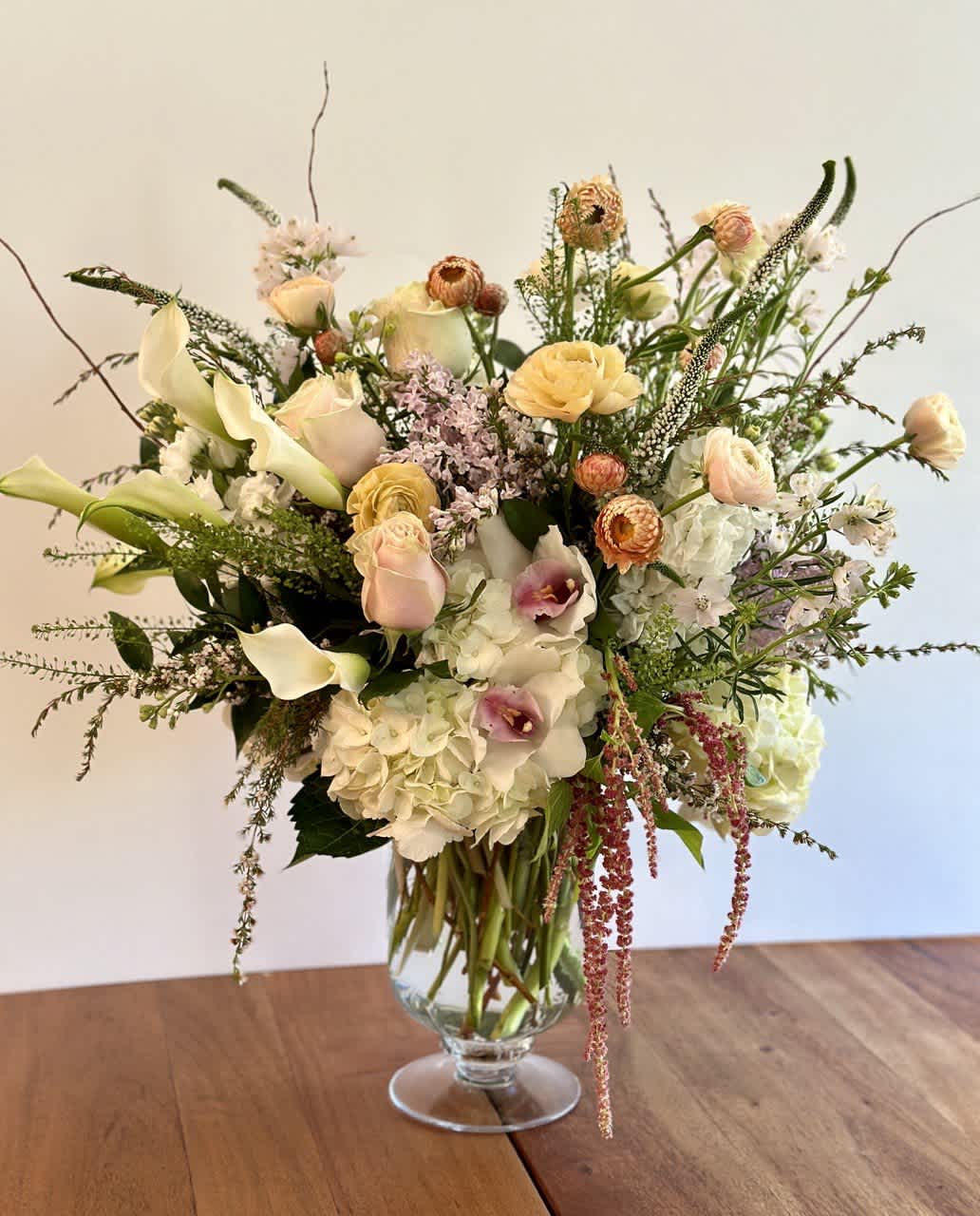 Tall arrangement of white hydrangeas, calla lilies, and pastel roses in a clear glass vase
