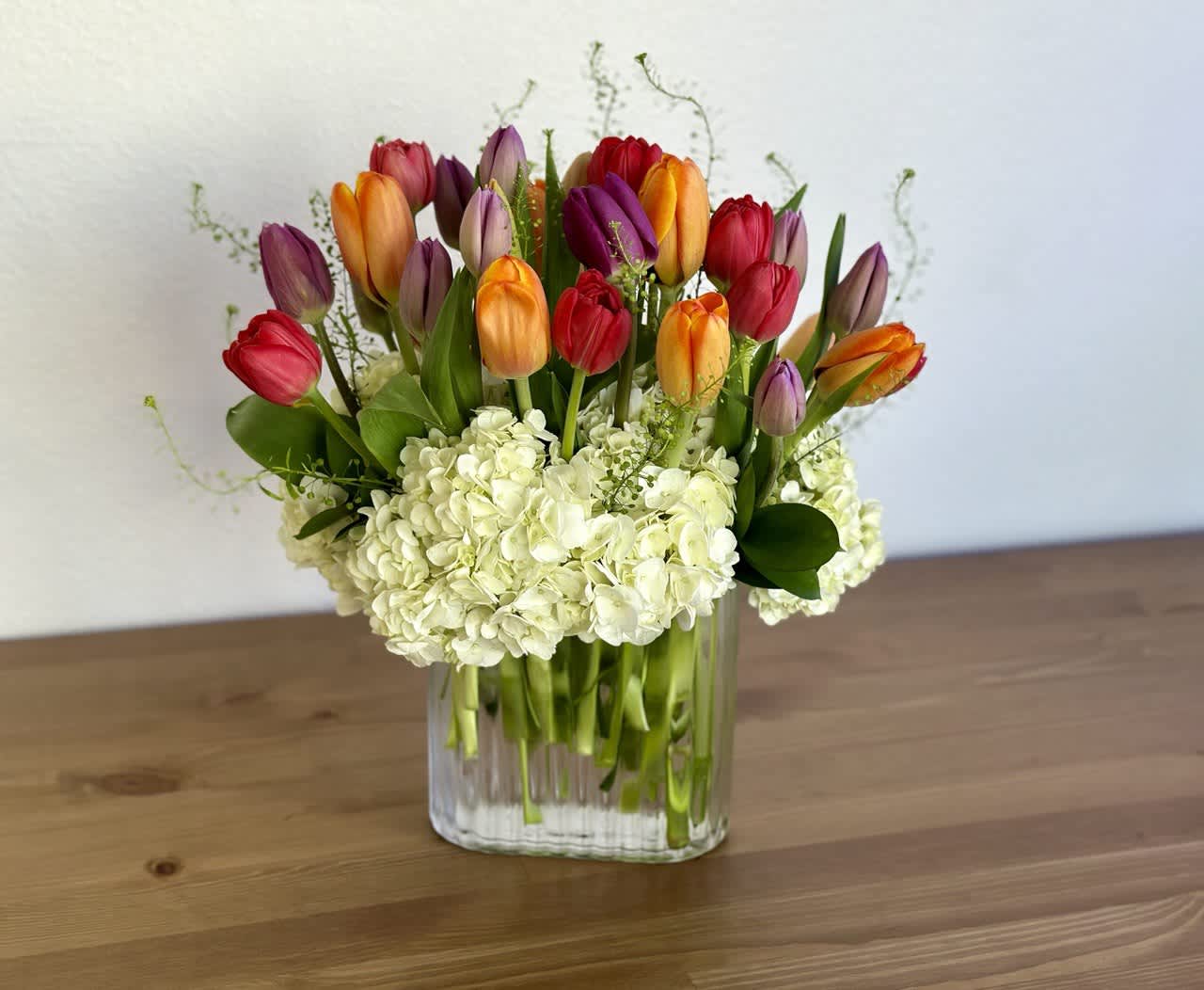 Colorful tulips arranged in a clear glass vase with white hydrangeas
