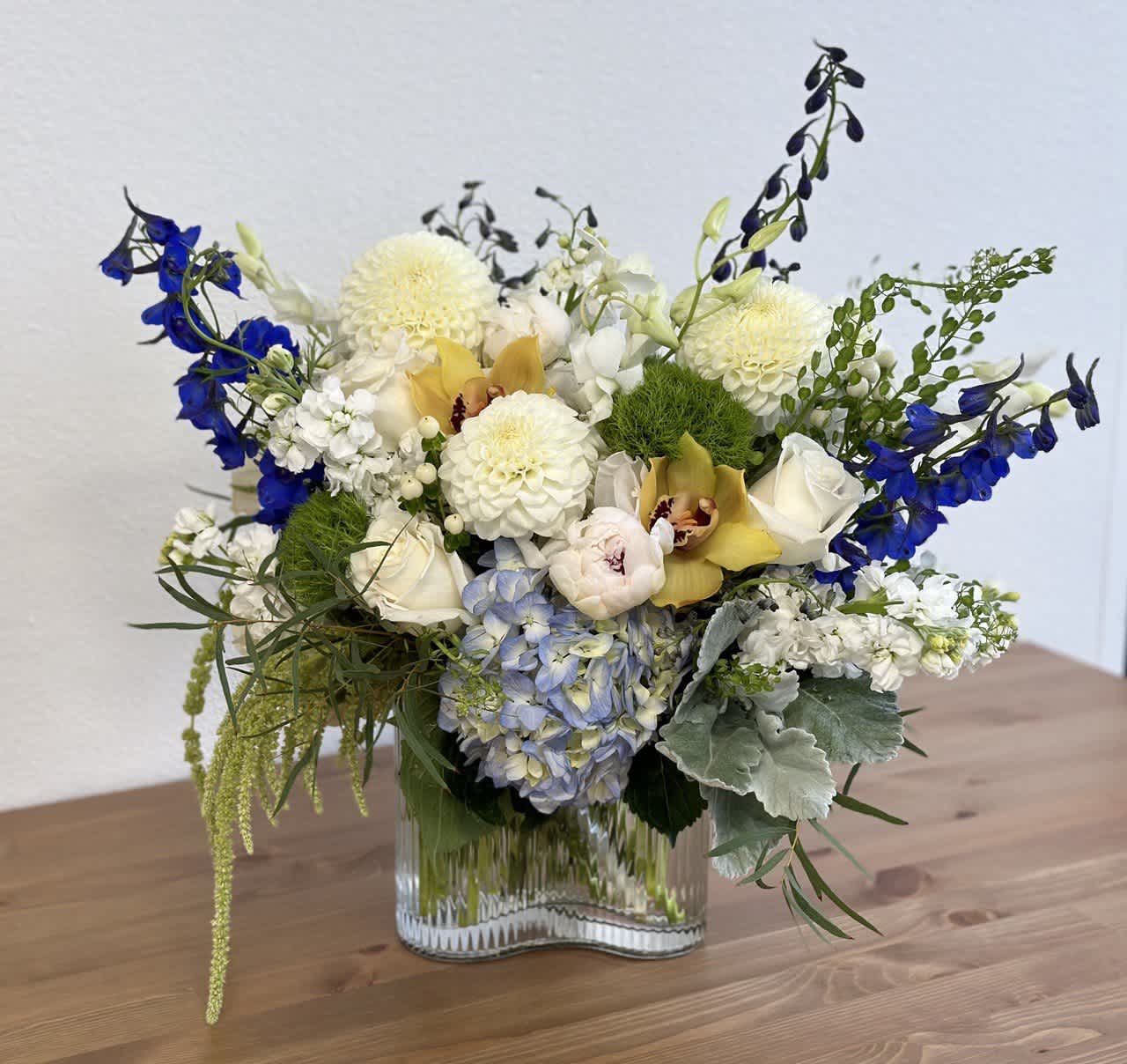 Mixed bouquet in a clear glass vase with blue, white, and yellow flowers